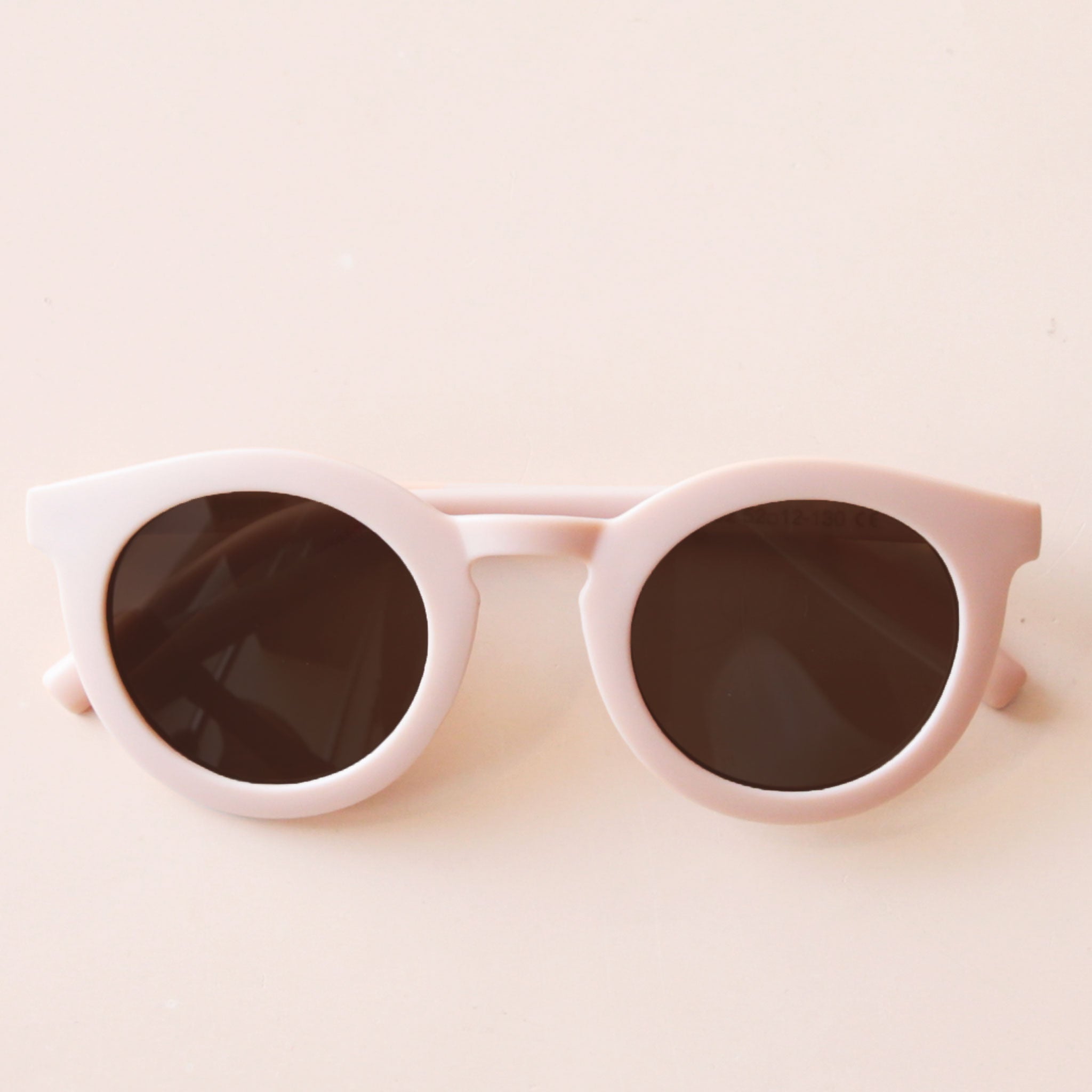 On a neutral background is a light pink children&#39;s sunglass with a round shape. 