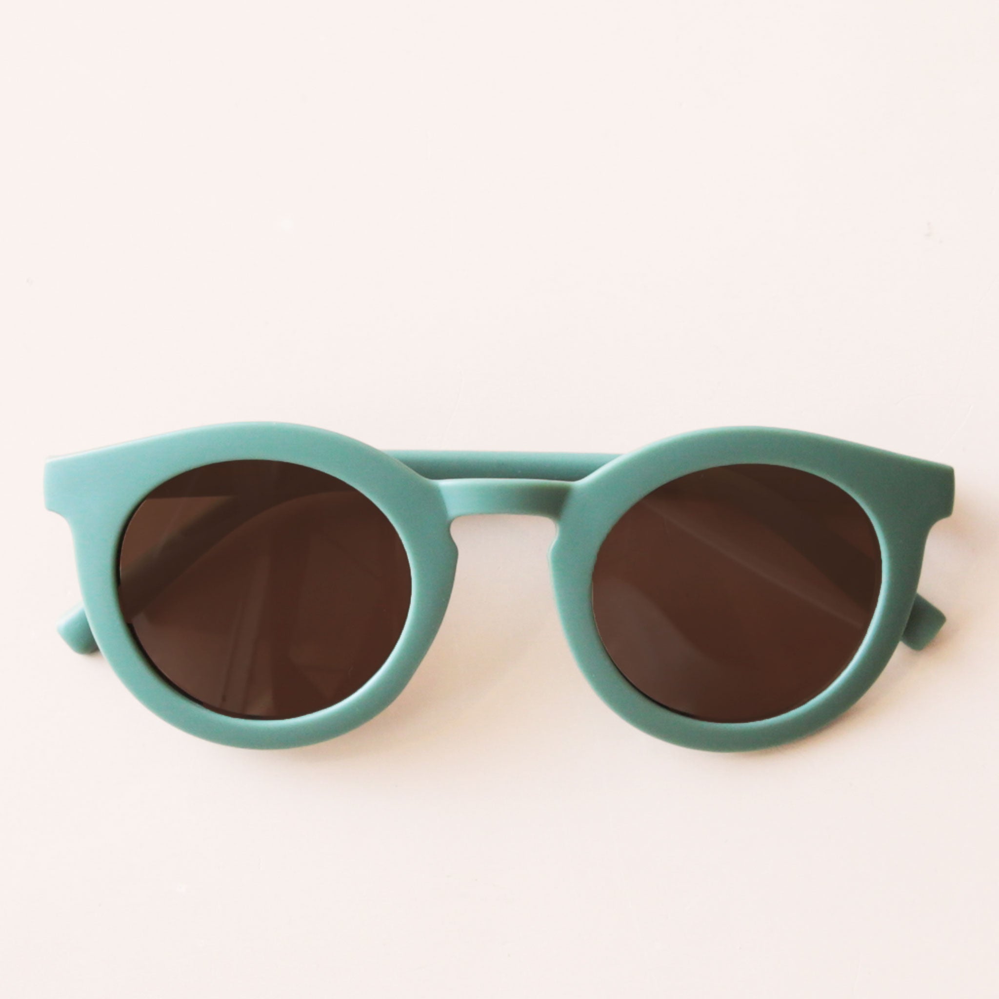 On a neutral background is a green pair of circle shape children&#39;s sunglasses. 