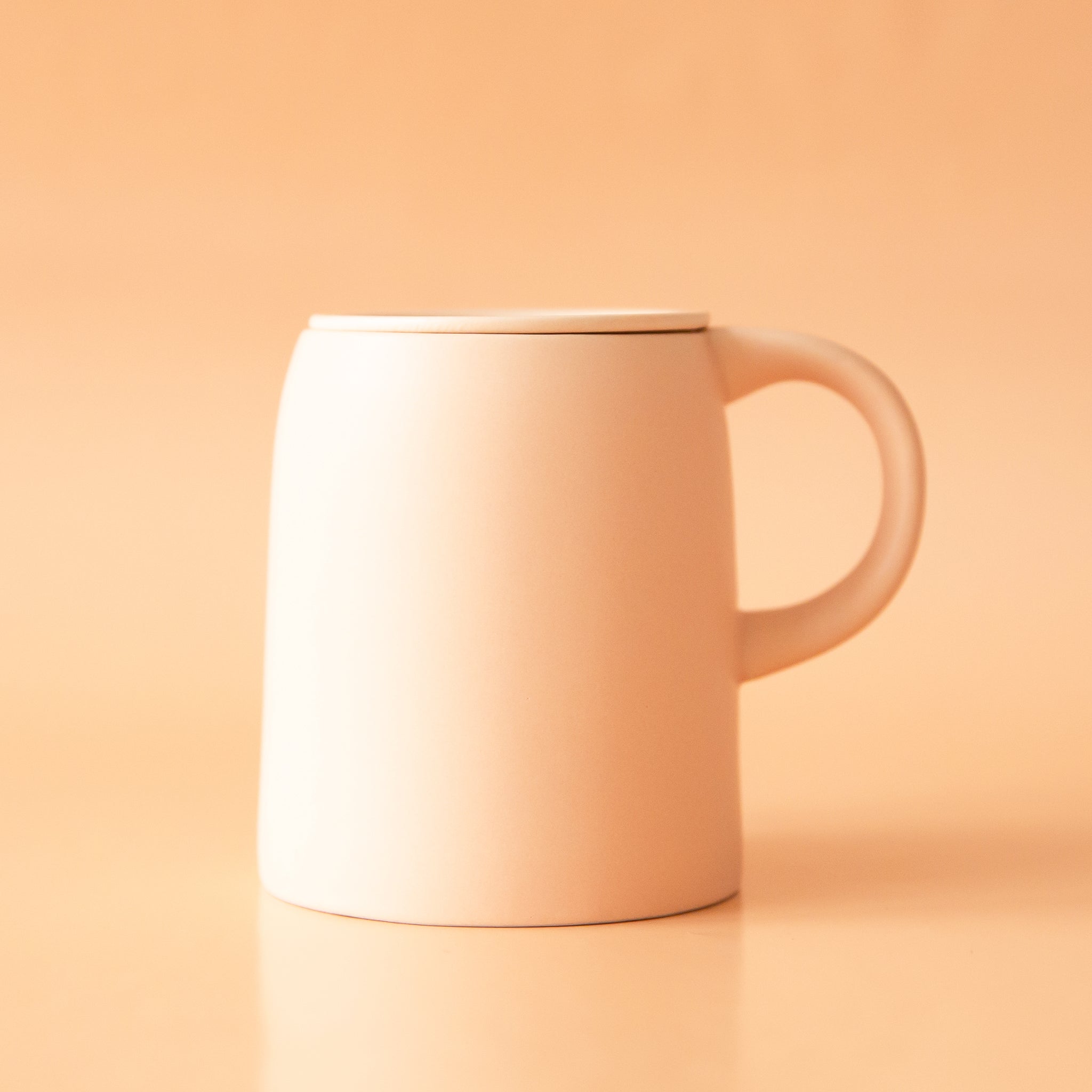 On a neutral background is a ceramic mug with an infuser cup to insert inside the rim of the mug.