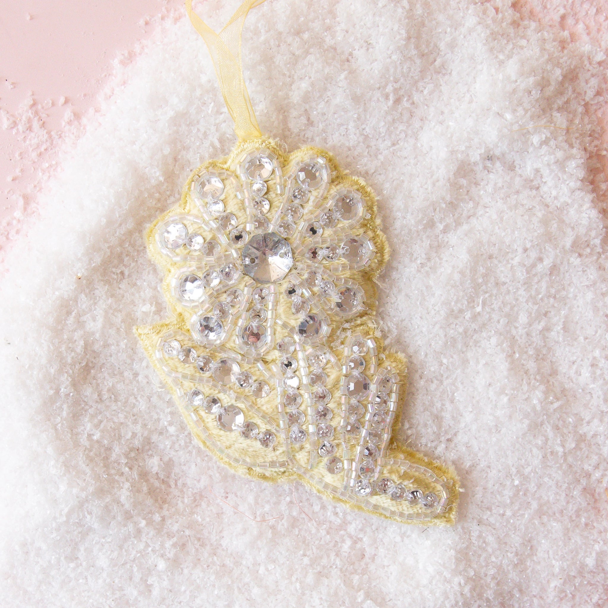 On a pink snowy background is a yellow flower shaped ornament with rhinestones. 