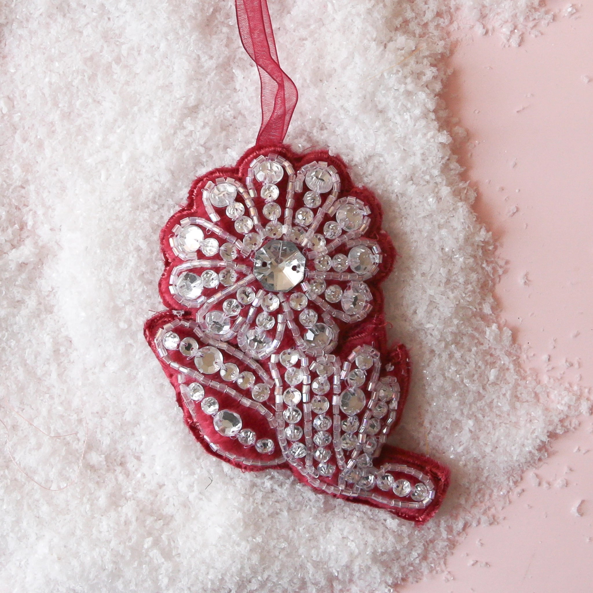 On a pink snowy background is a maroon flower shaped ornament with rhinestones all over.