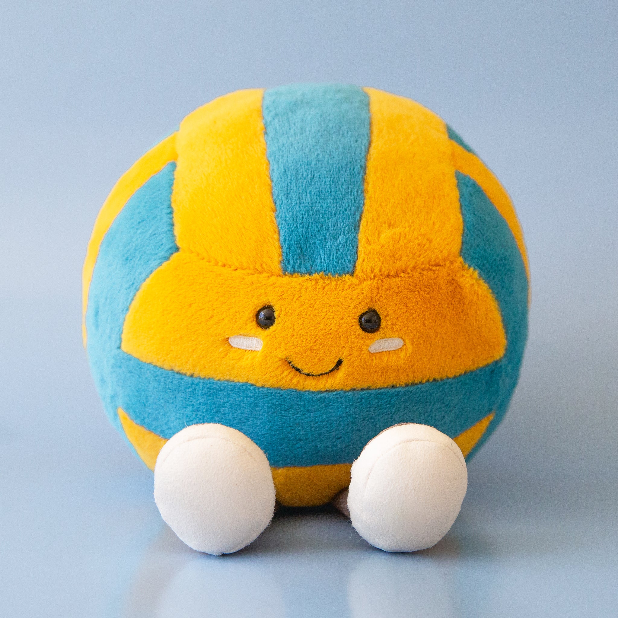 A blue and yellow stuffed toy in the shape of a volleyball with adorable legs, feet and a smiling face.