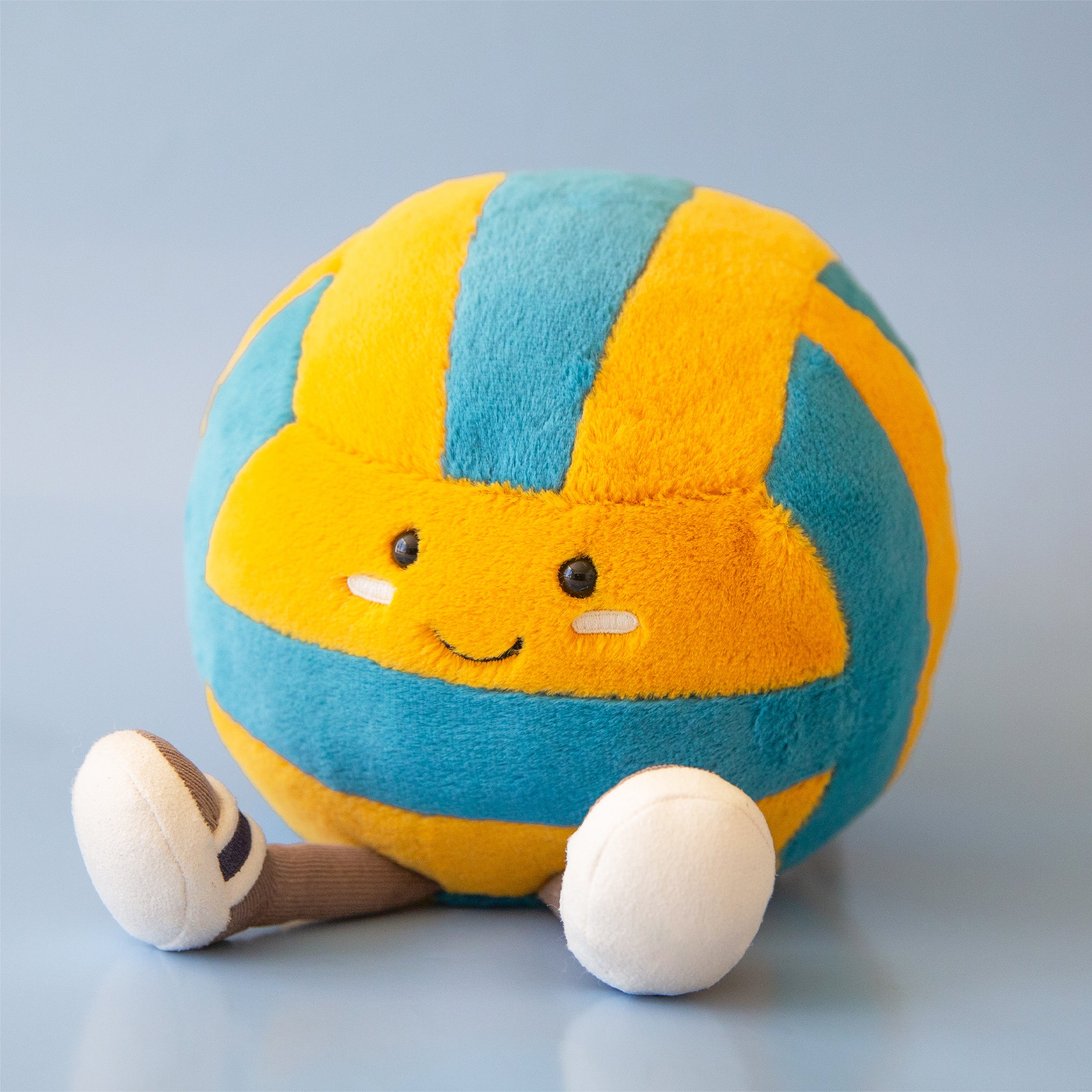 A blue and yellow stuffed toy in the shape of a volleyball with adorable legs, feet and a smiling face.