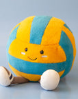 A blue and yellow stuffed toy in the shape of a volleyball with adorable legs, feet and a smiling face.