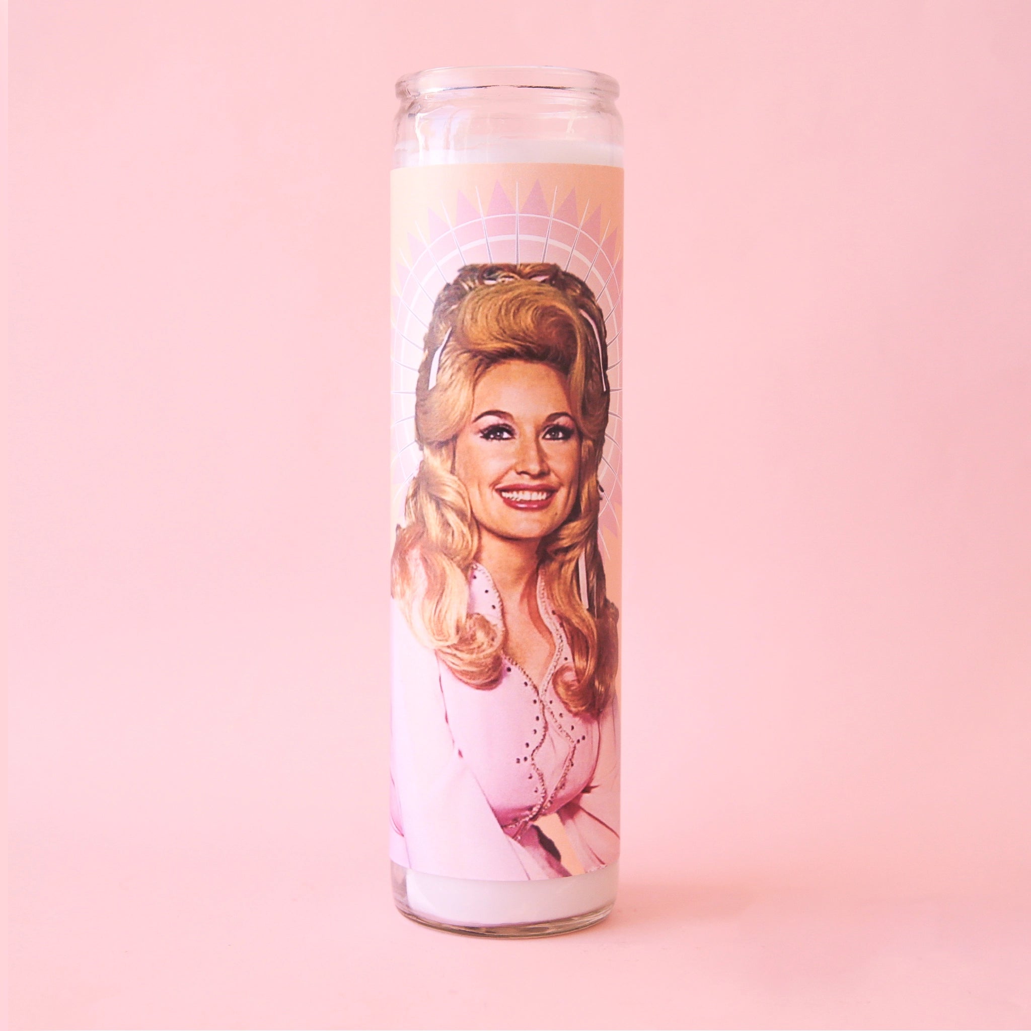 A tall glass prayer candle. On the front is a picture of Dolly Parton with long blonde hair and a pink jacket. 