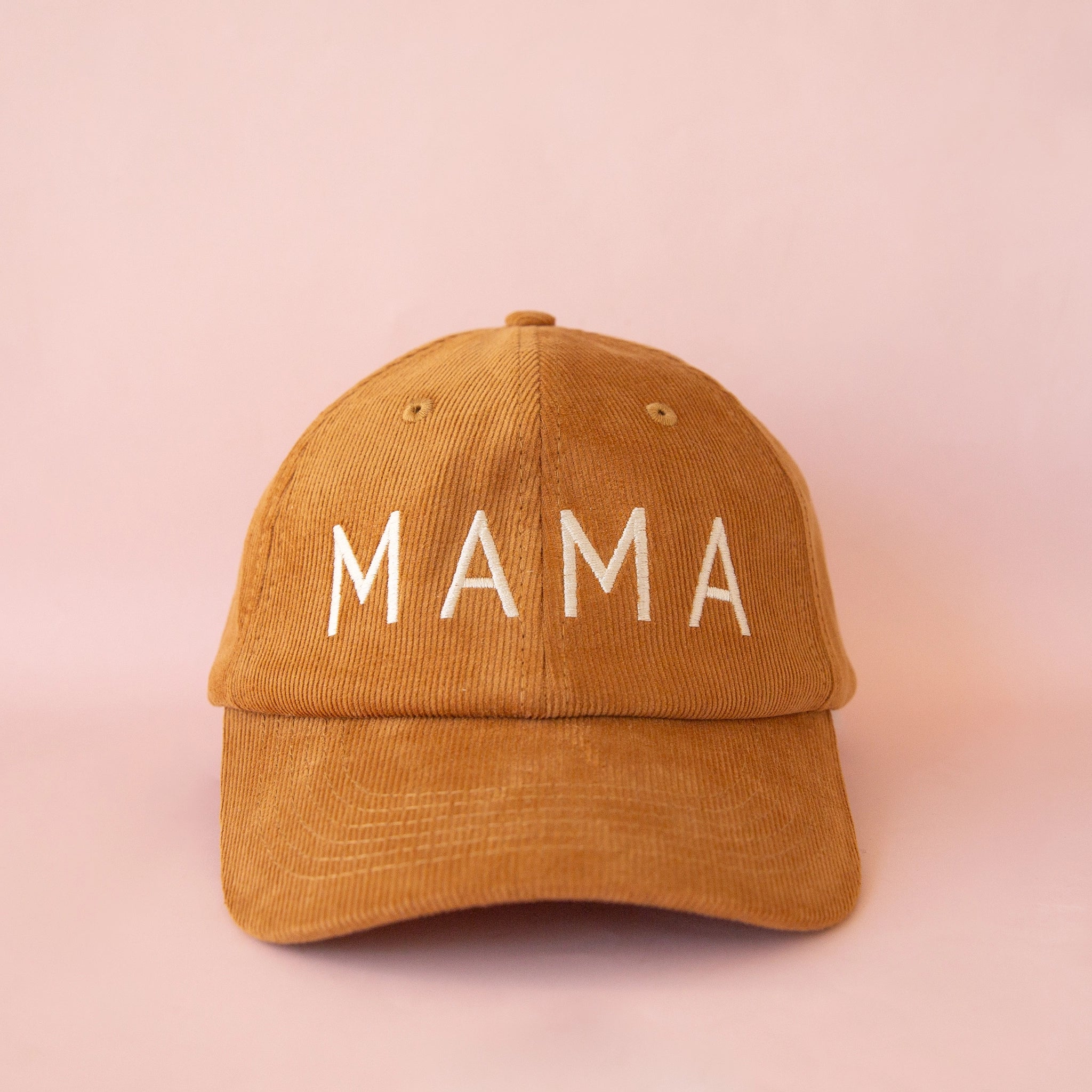 On a pink background is a toffee colored corduroy baseball hat with white embroidered text on the front that reads, &quot;MAMA&quot;.