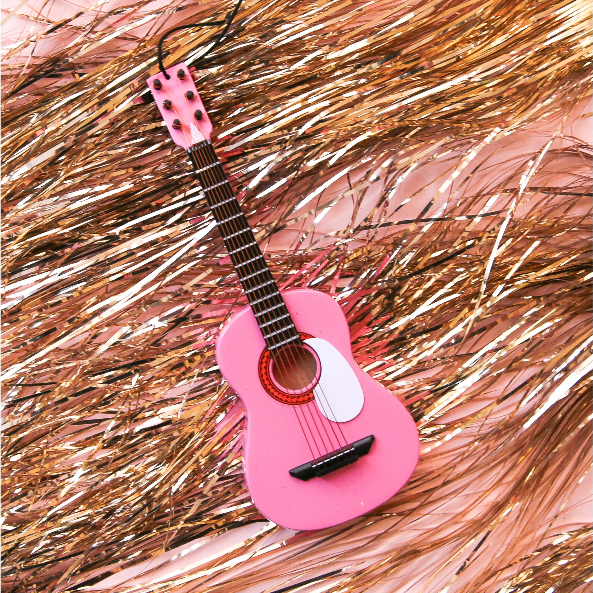 On a pink and gold tinsel background is a pink guitar ornament. 