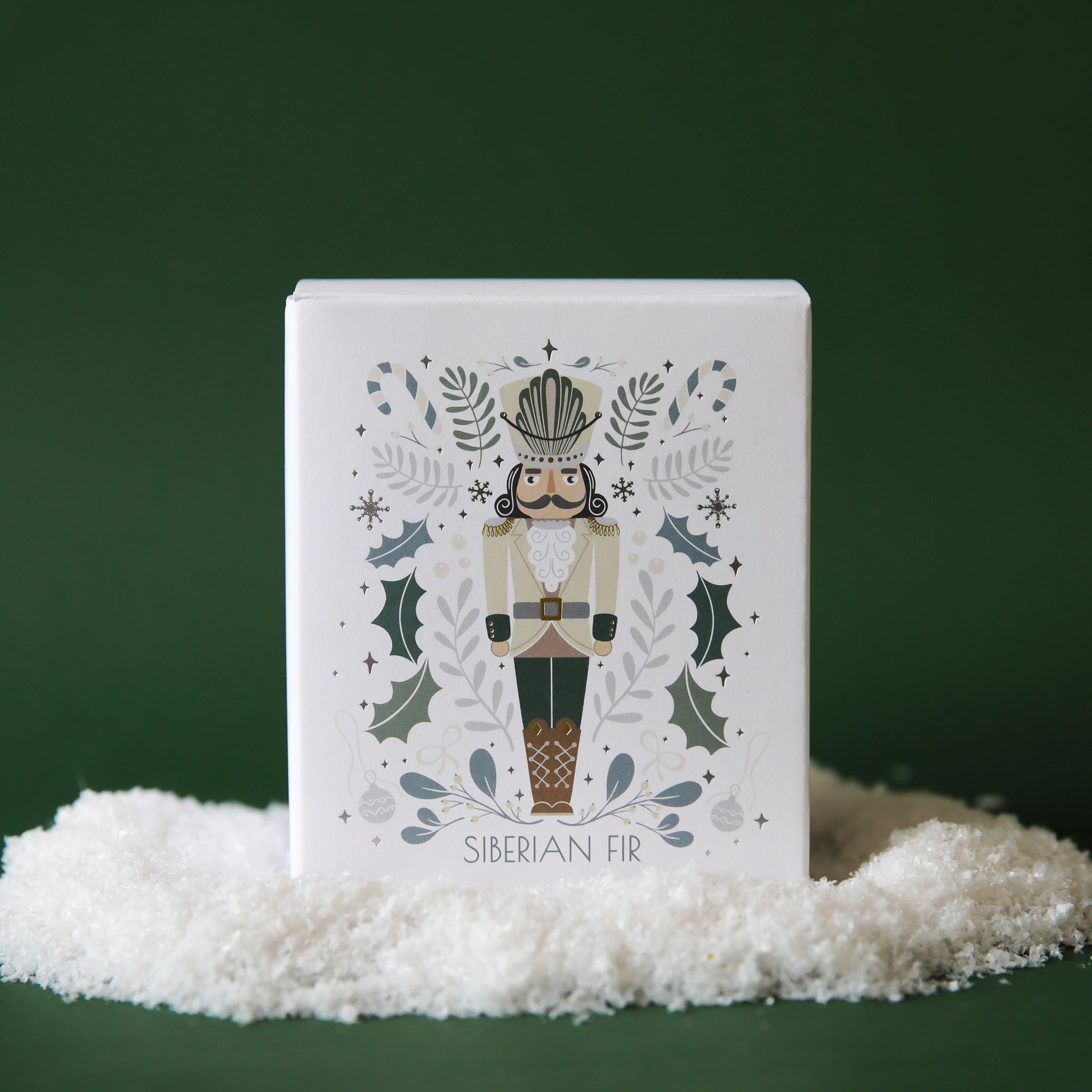 On a green background is a white boxed candle with a picture of a nutcracker on the front. 
