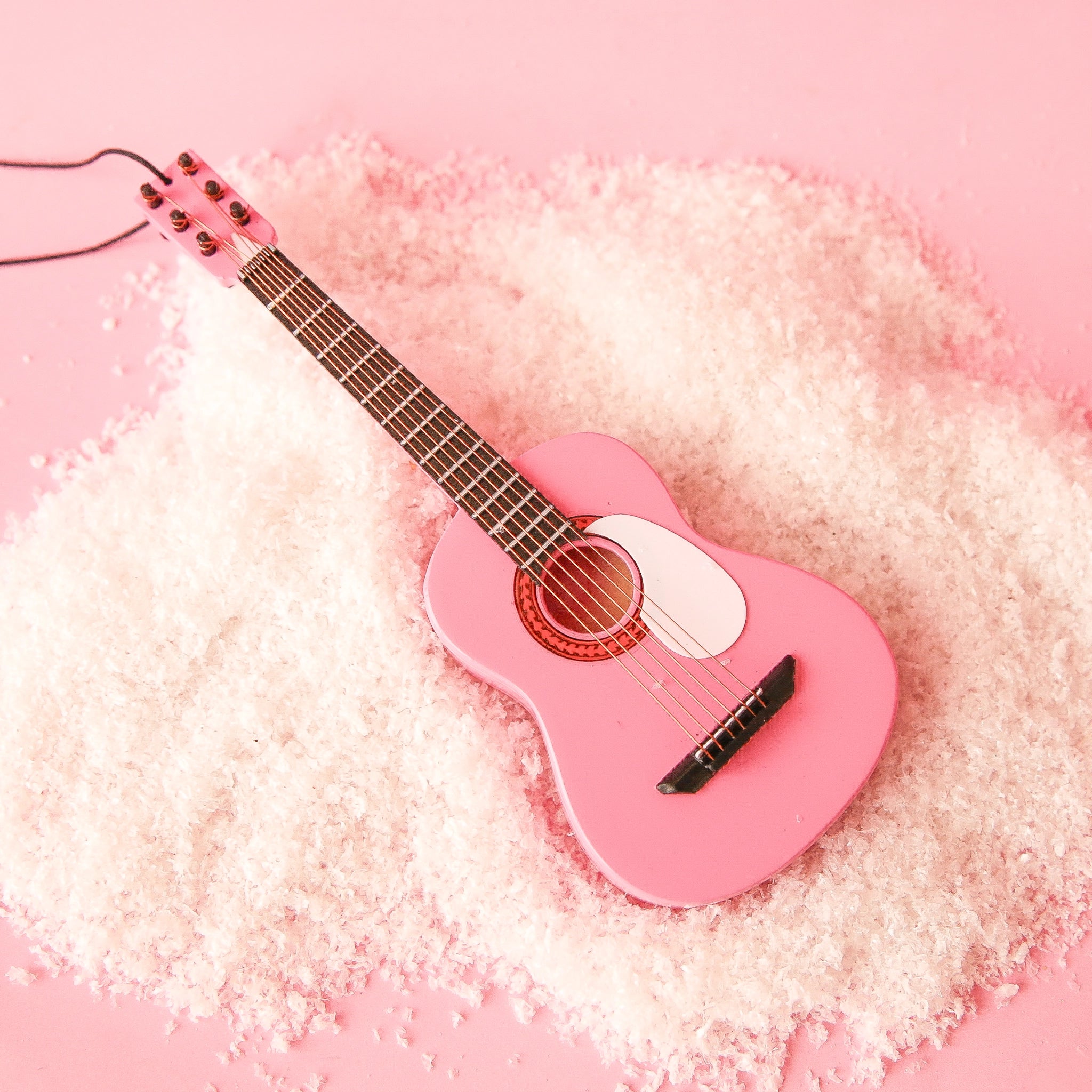 On a pink snowy background is a pink string guitar ornament. 