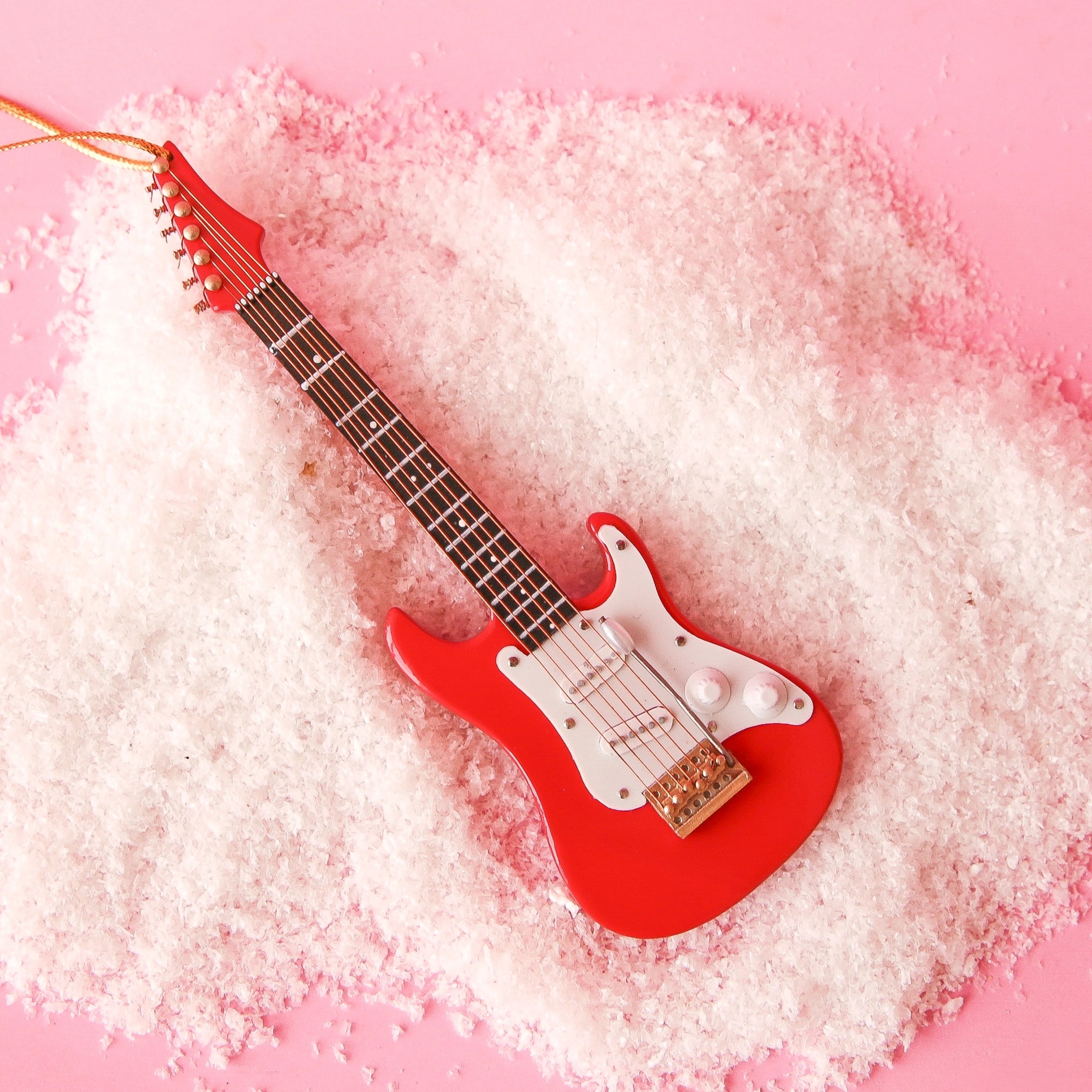 On a pink snowy background is a red and white electric guitar ornament.