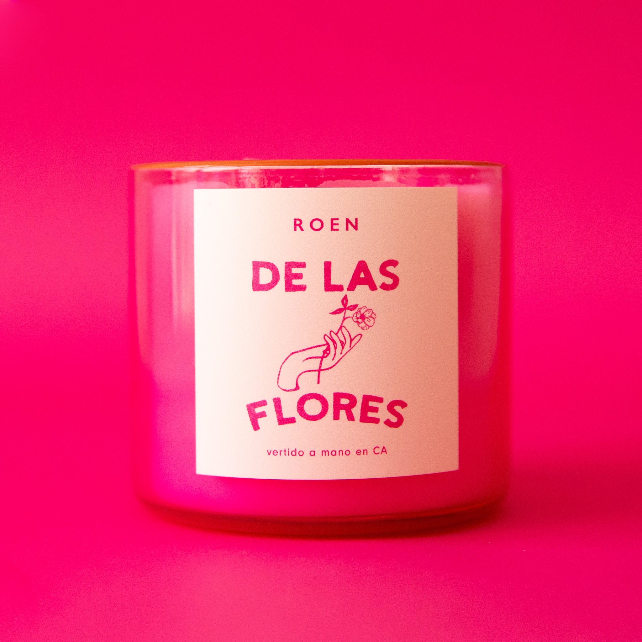 A hot pink glass candle with a label on the front that reads, "De Las Flores".
