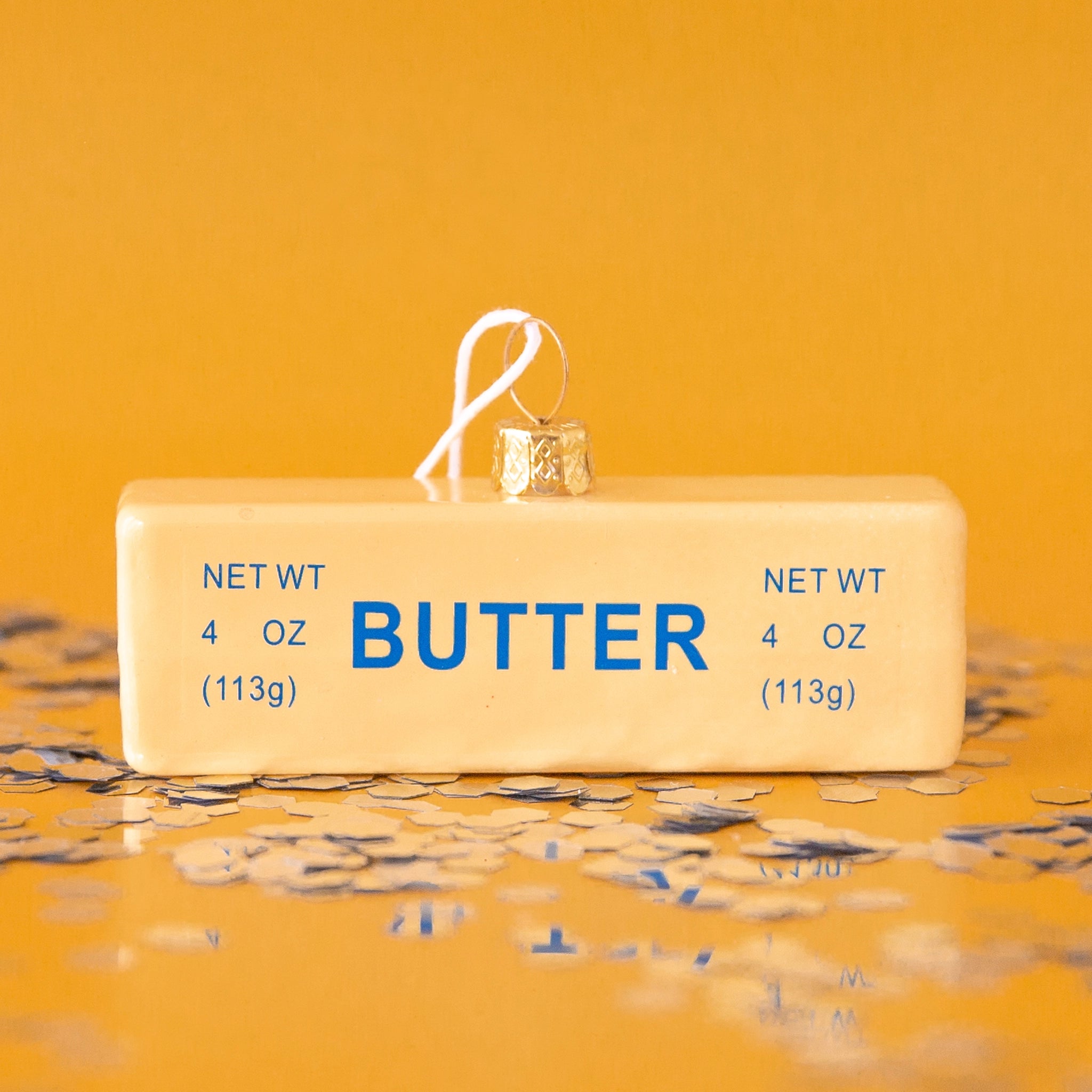 On a yellow background is a glass ornament in the shape of a stick of butter
