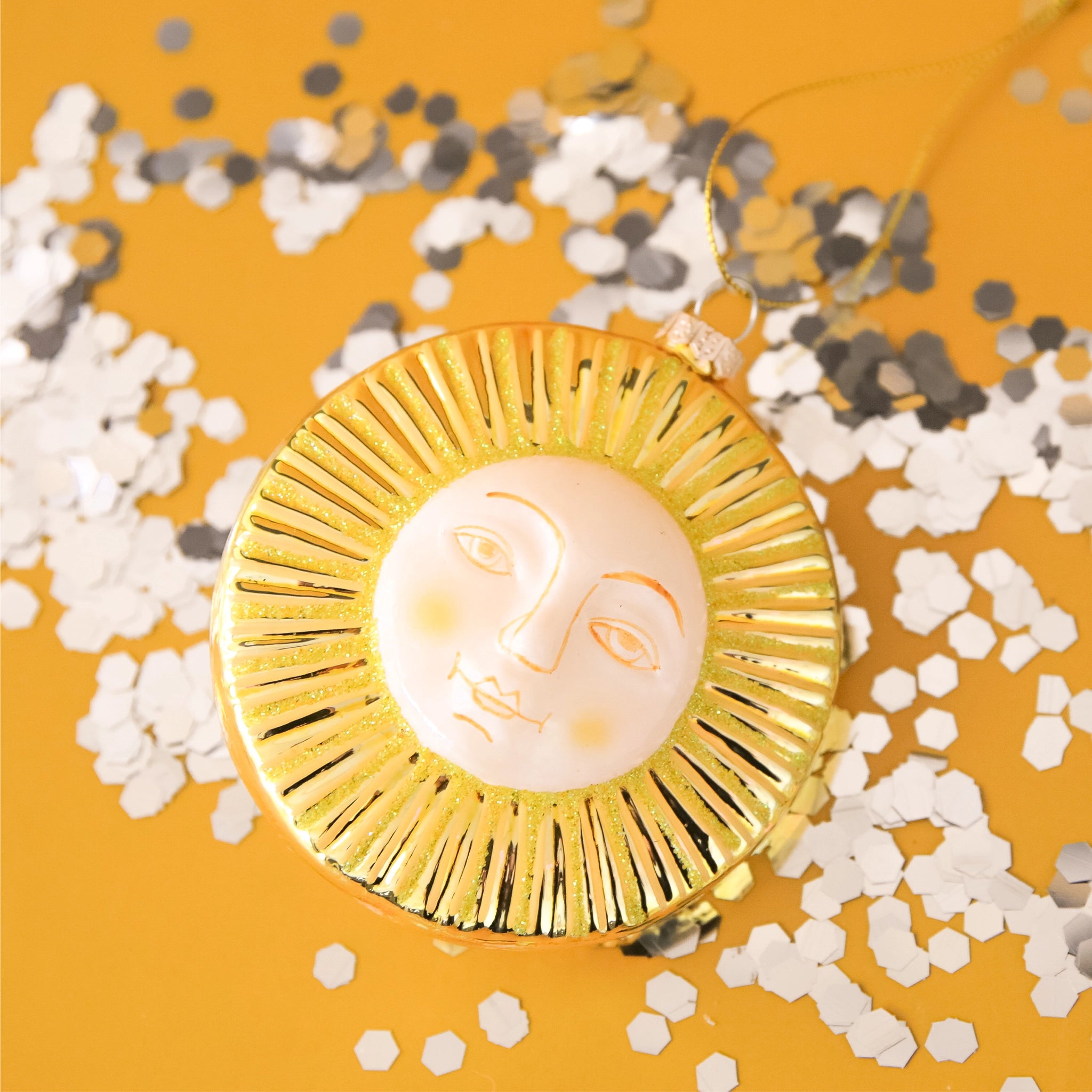 Glass sun ornament features gold rays surrounding a white face.