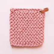 On a white background is a pink crocheted pot holder with a leather loop at the top right corner. 