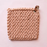 On a light pink background is a terracotta colored crocheted pot holder with a leather loop in the top right corner. 