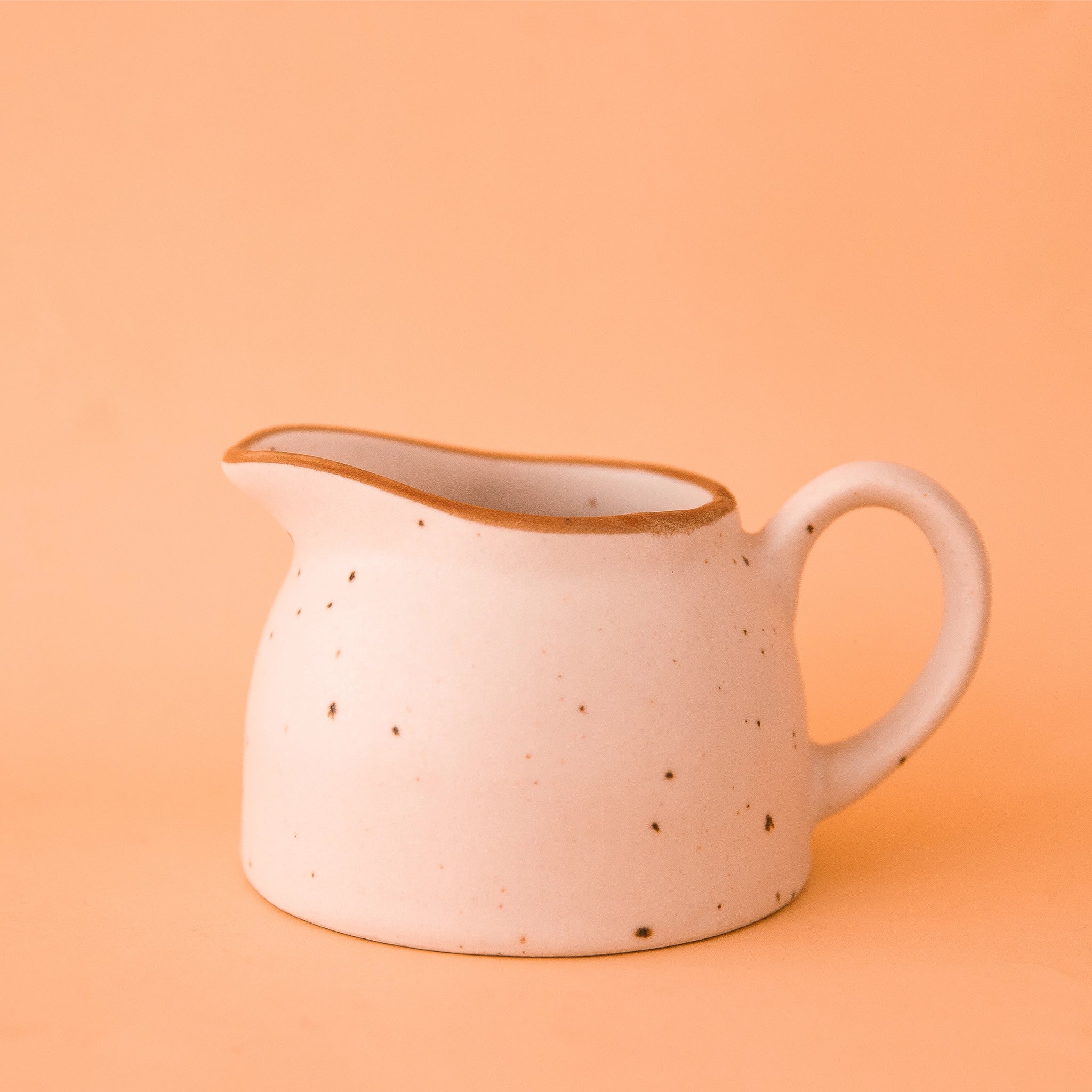 On a peachy background is a cream colored stoneware carafe with a tan rim around the edge.