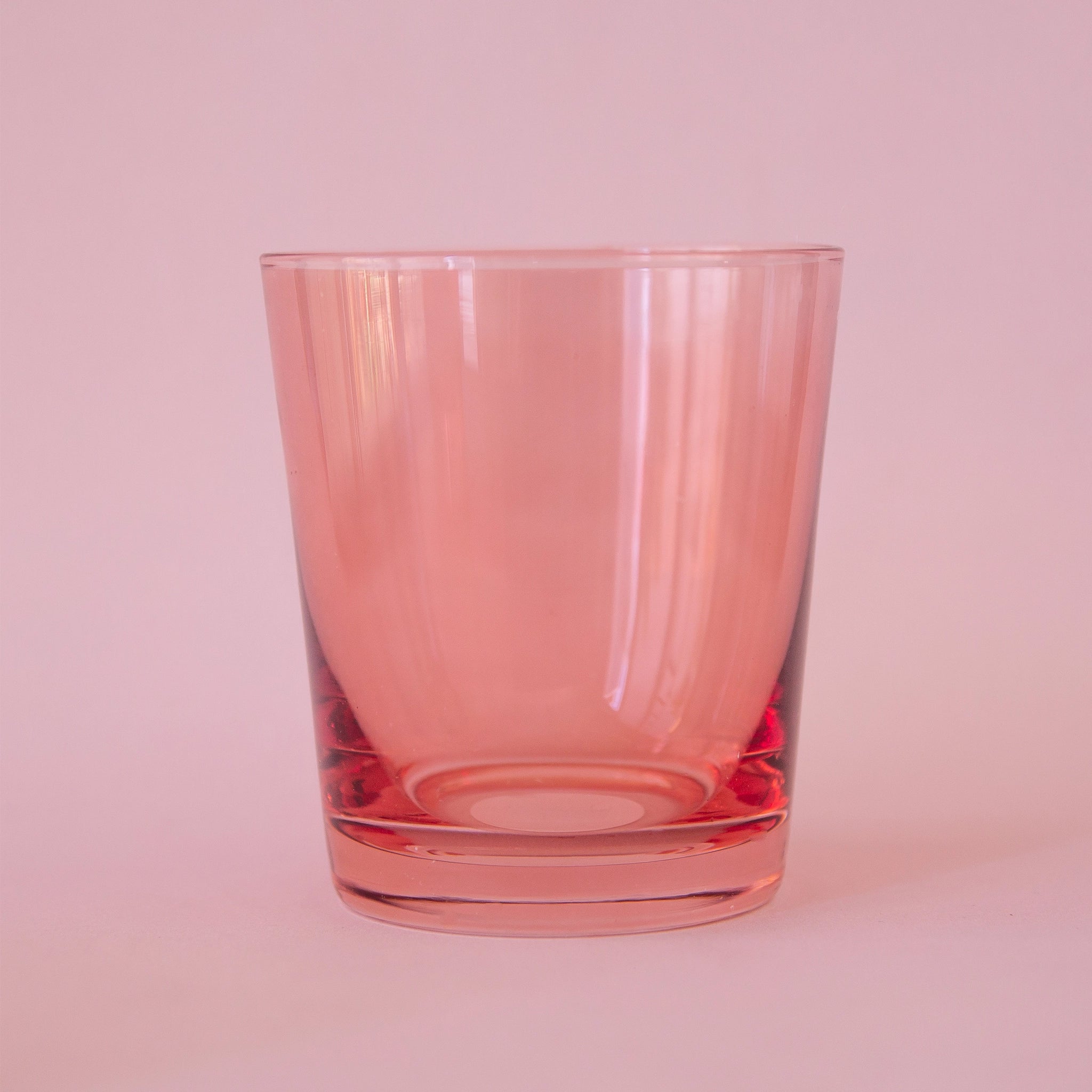 On a pink background is a short low ball drinking glass in a pink shade. 