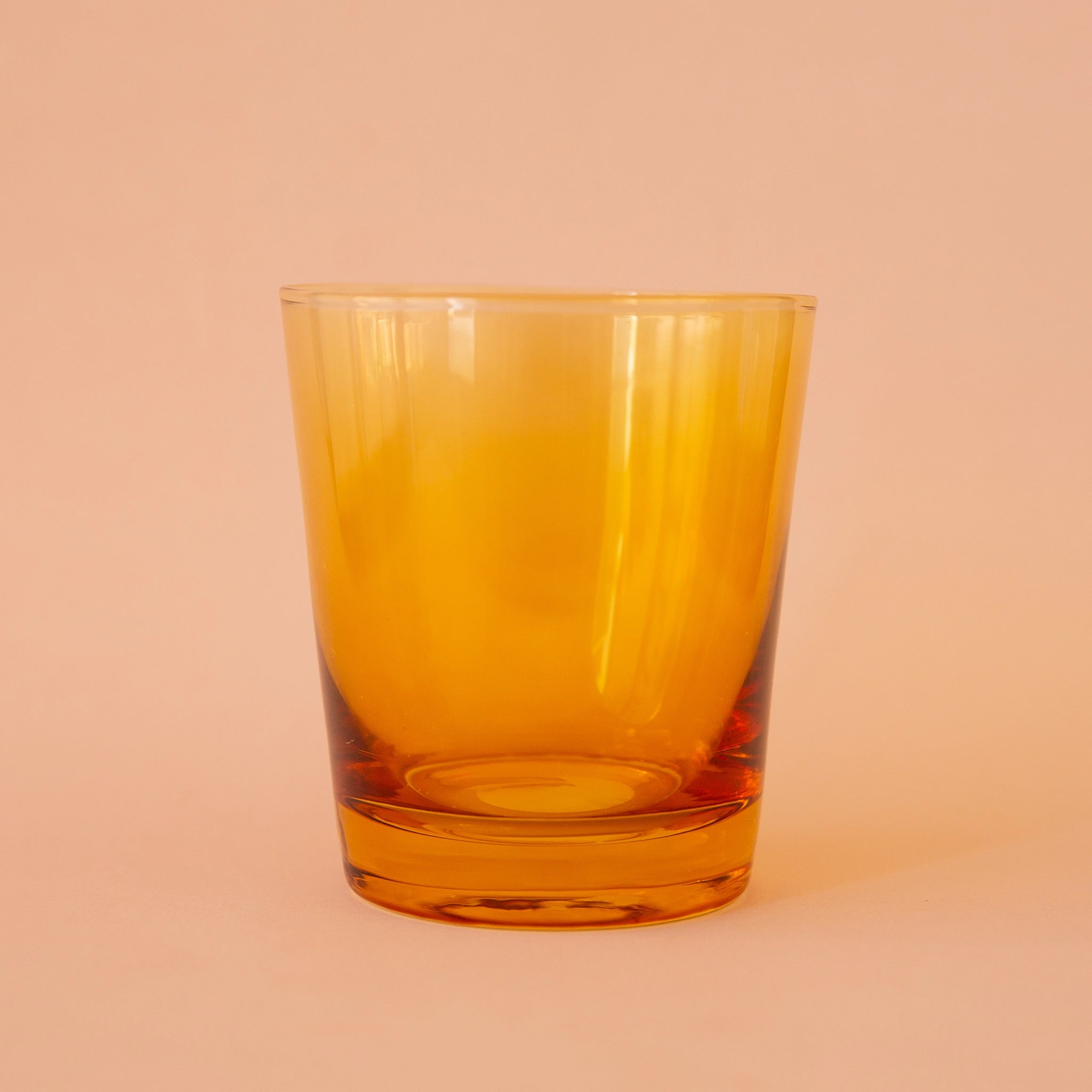 On a peachy background is a short yellow drinking glass. 