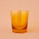 On a peachy background is a short yellow drinking glass. 