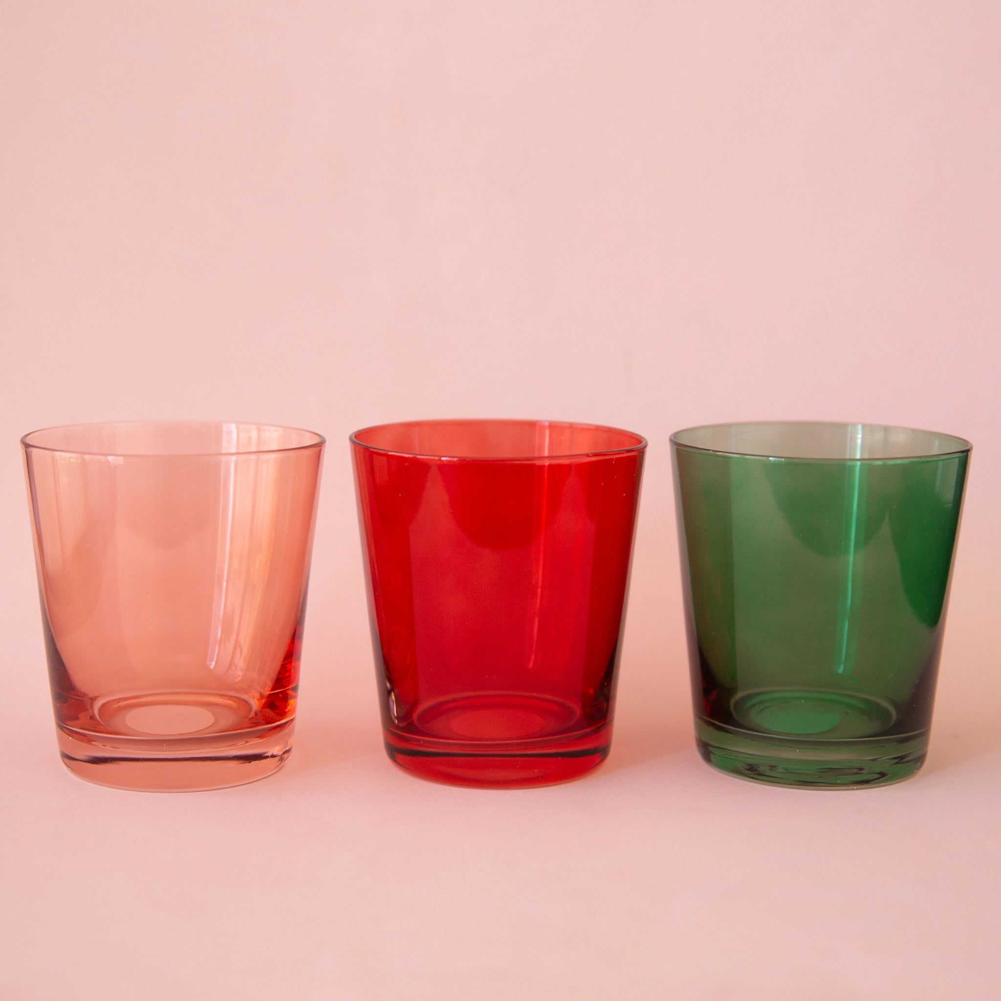 Three lowball drinking glasses featuring the other three color options for this glass. There is a pink, red and green option.