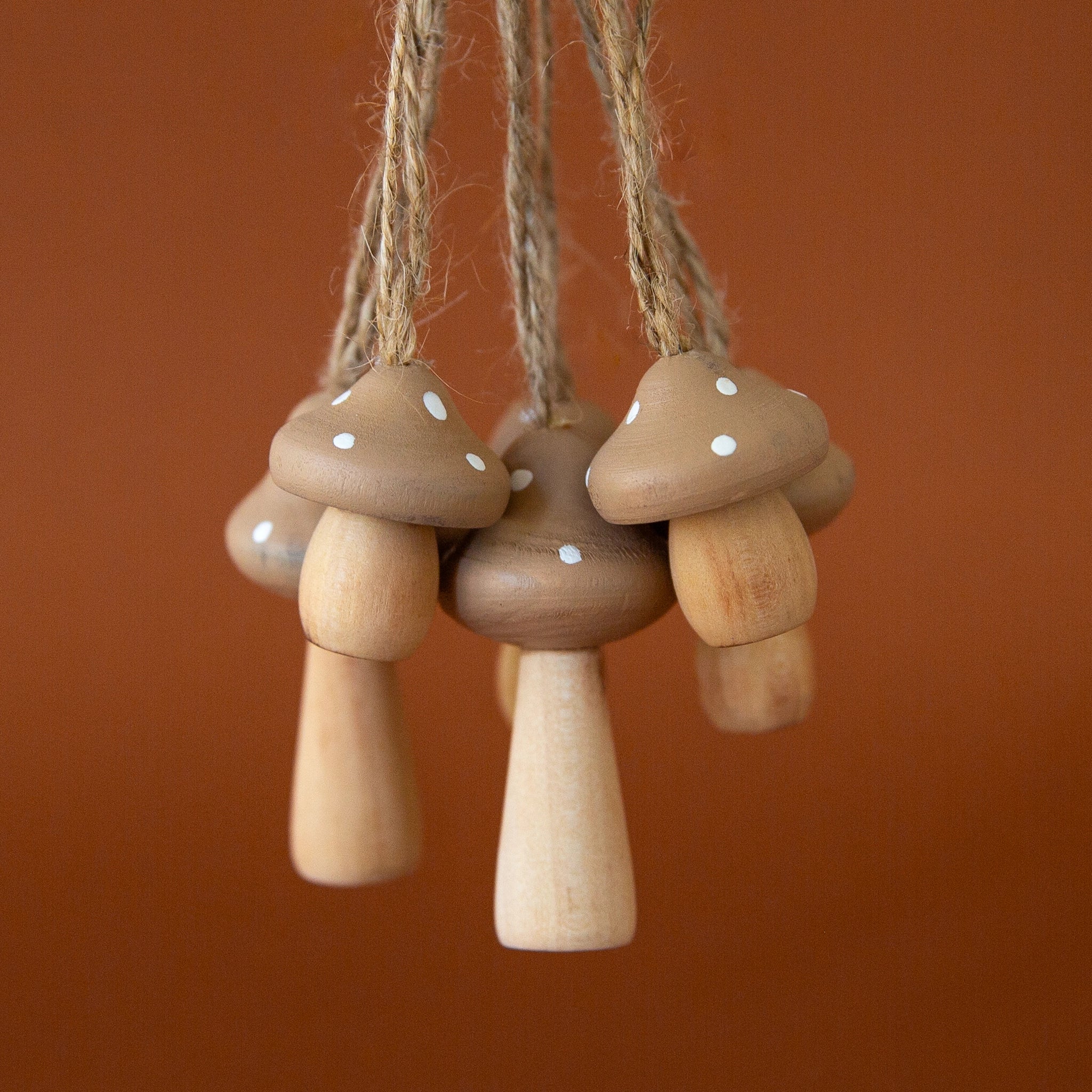 On a burnt orange background is six wooden mushroom shaped ornaments with a twine loop for hanging. 