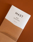 A rectangular bar of chocolate that read, "Mast Milk Chocolate" at the top in black letters along with a two toned wrapper that is brown and white.