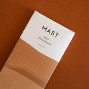 A rectangular bar of chocolate that read, "Mast Milk Chocolate" at the top in black letters along with a two toned wrapper that is brown and white.