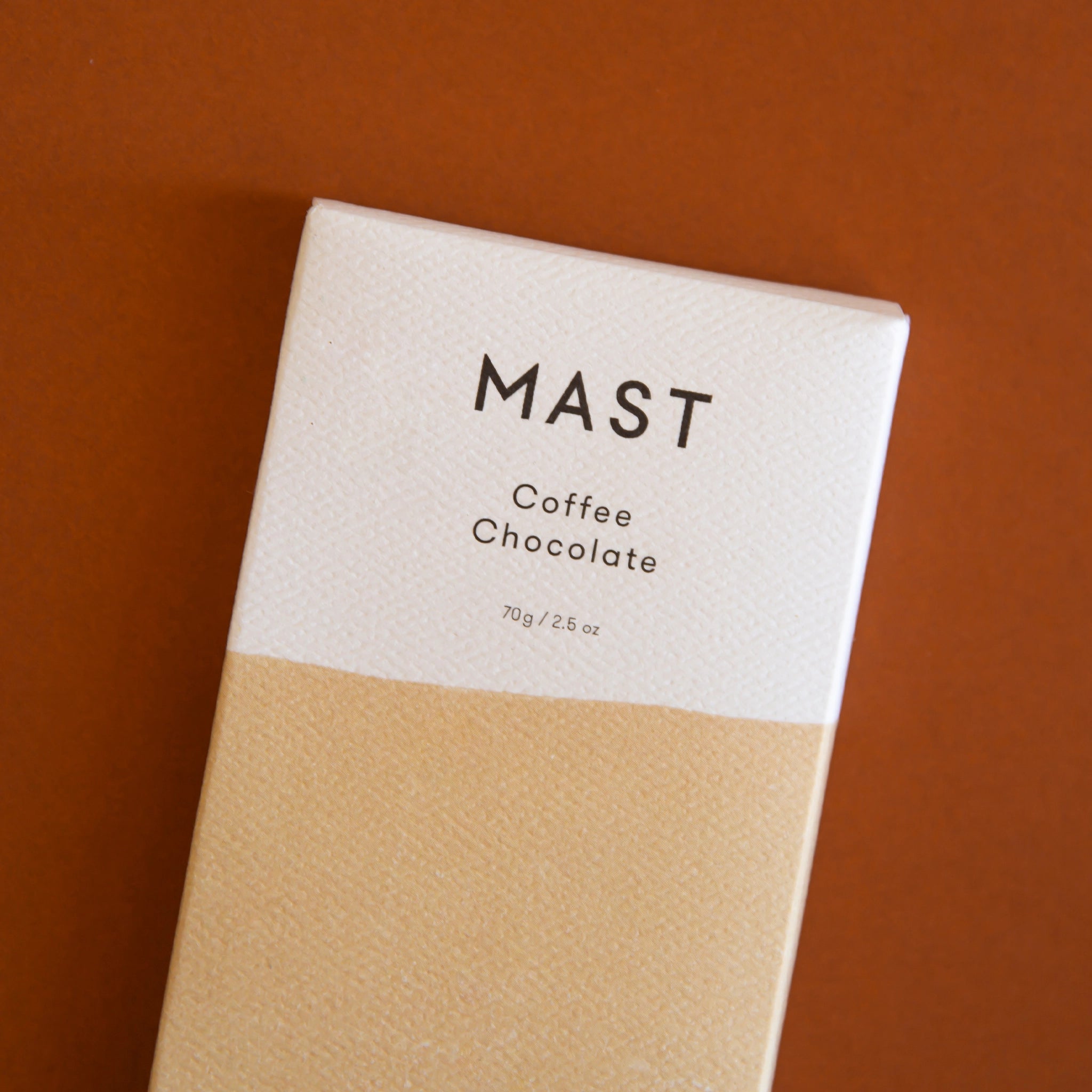 A rectangle chocolate bar packaged in a white and tan wrapper with black text that reads, &quot;MAST Coffee Chocolate&quot;.