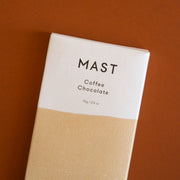 A rectangle chocolate bar packaged in a white and tan wrapper with black text that reads, "MAST Coffee Chocolate".