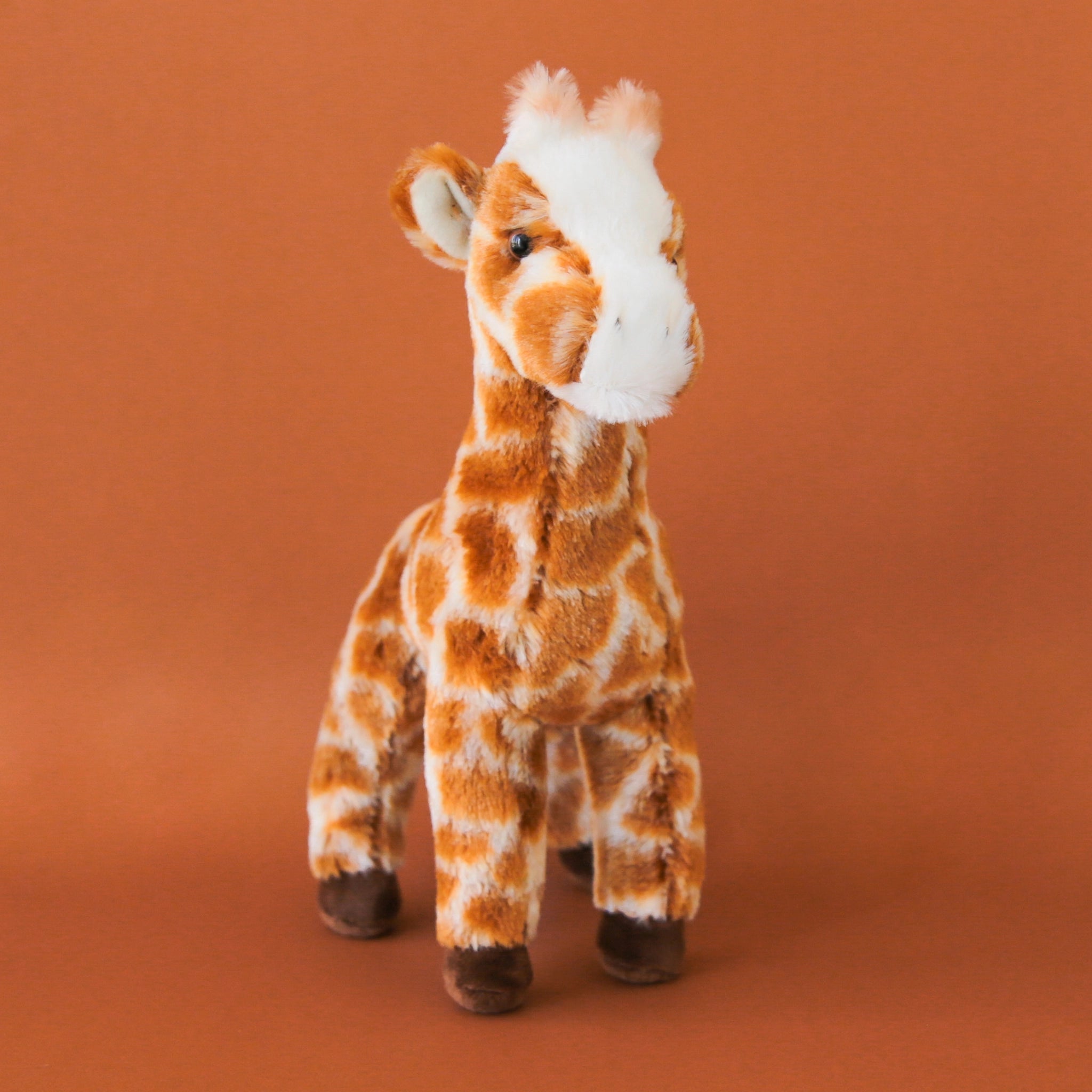 A brown and white giraffe stuffed animal toy with chocolate brown hooves.