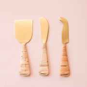 Gold cheese knives wrapped with natural rattan handles. A hatched design is on one side of the knives, while the opposite side is horizontally wrapped.