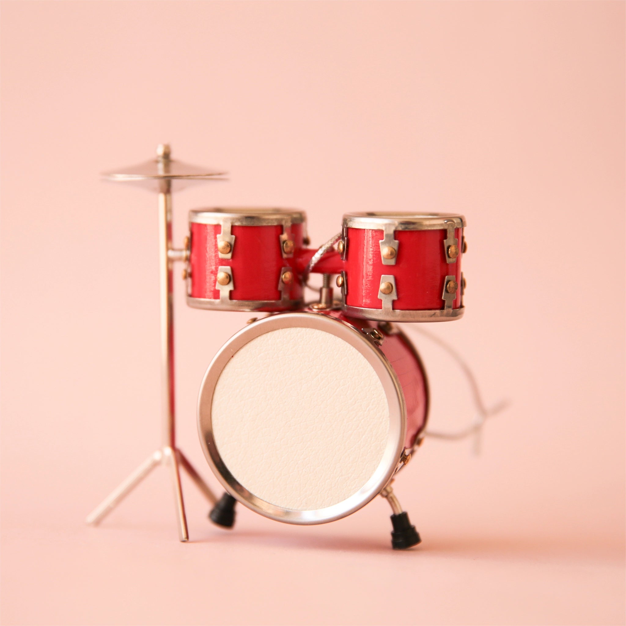 On a pink background is a red drum set shaped ornament. 