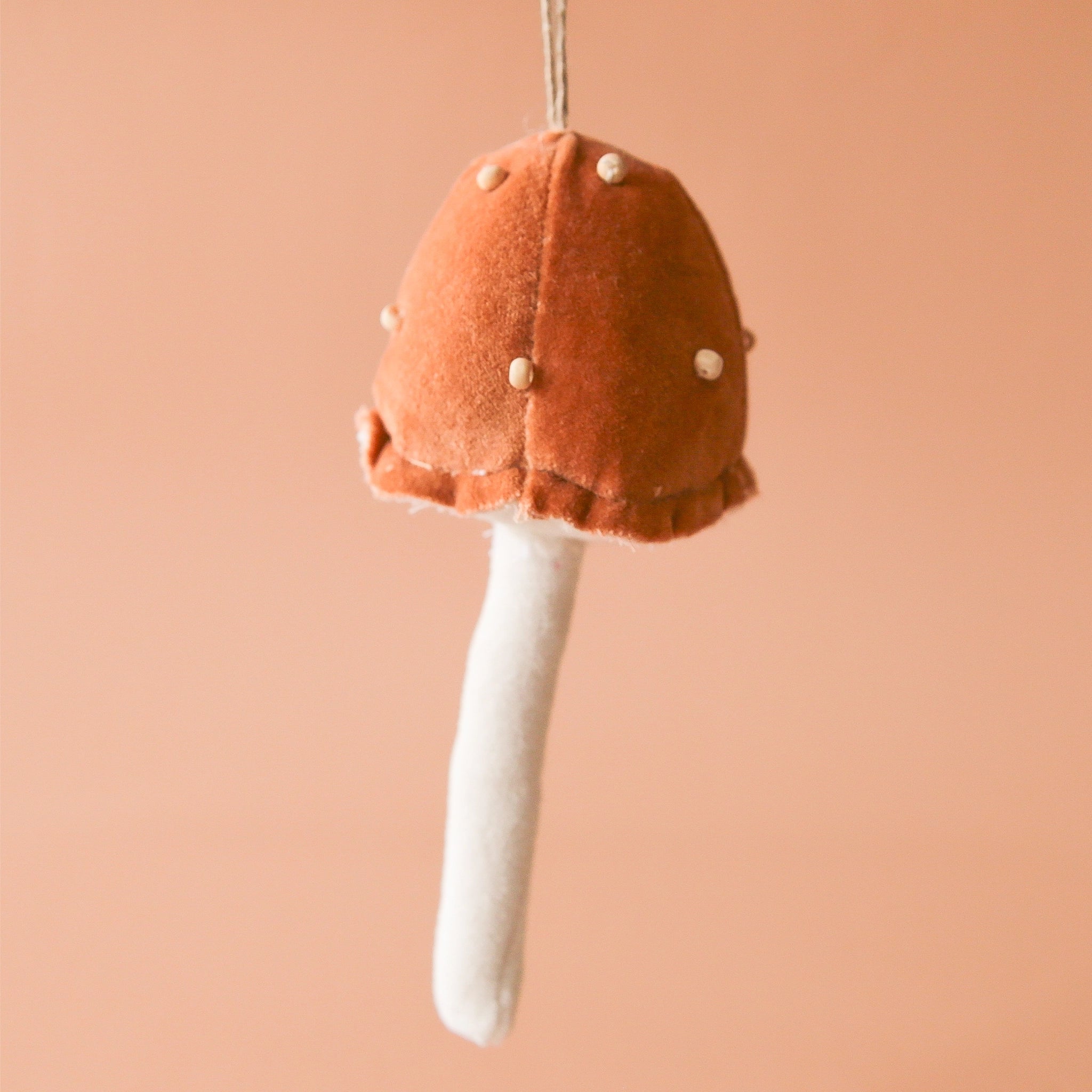 On an orange background is a rust and white velvet mushroom ornament with white beads.