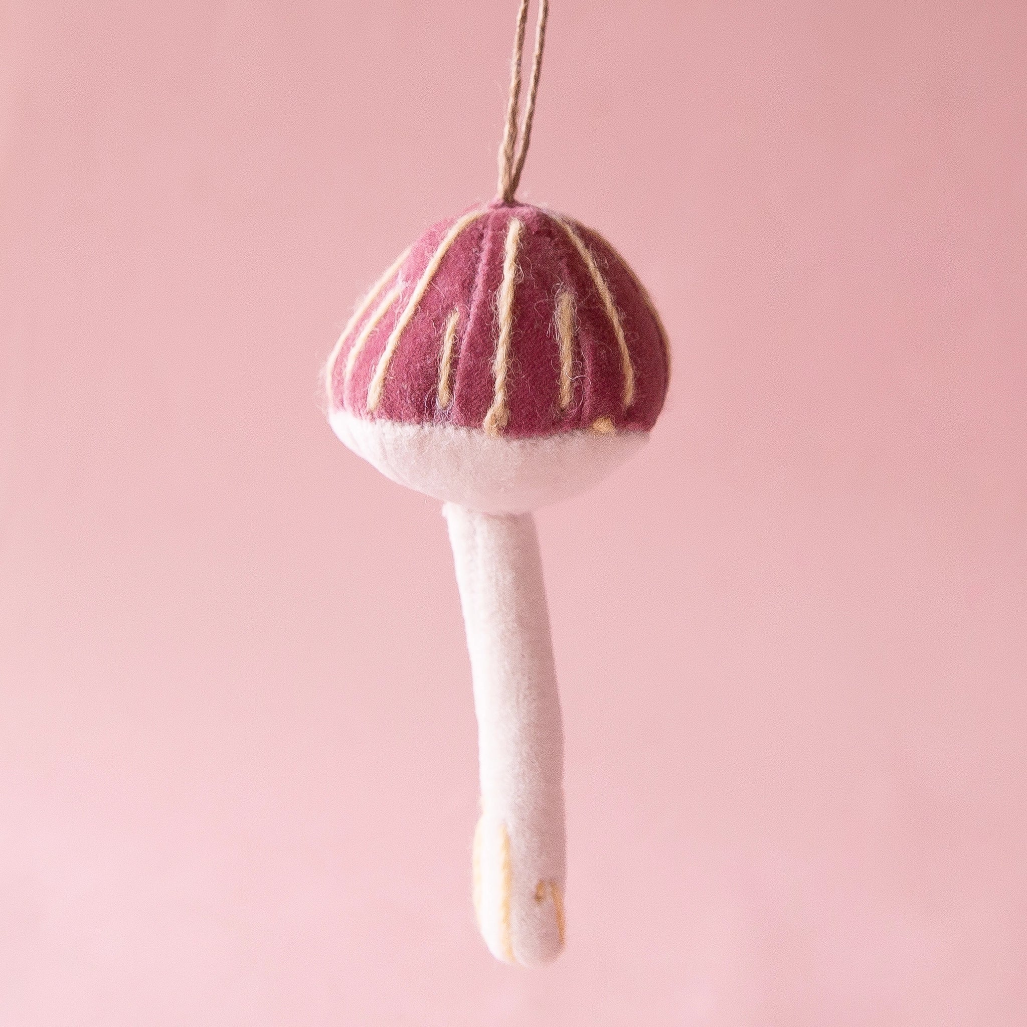 On a pink background is a maroon and white velvet mushroom ornament.