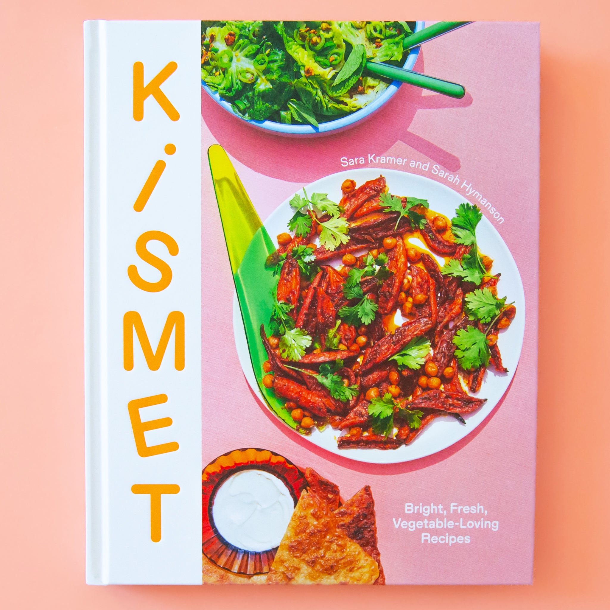 A pink book cover with photographs of three plates of food and the title along the left side that reads, "Kismet". 