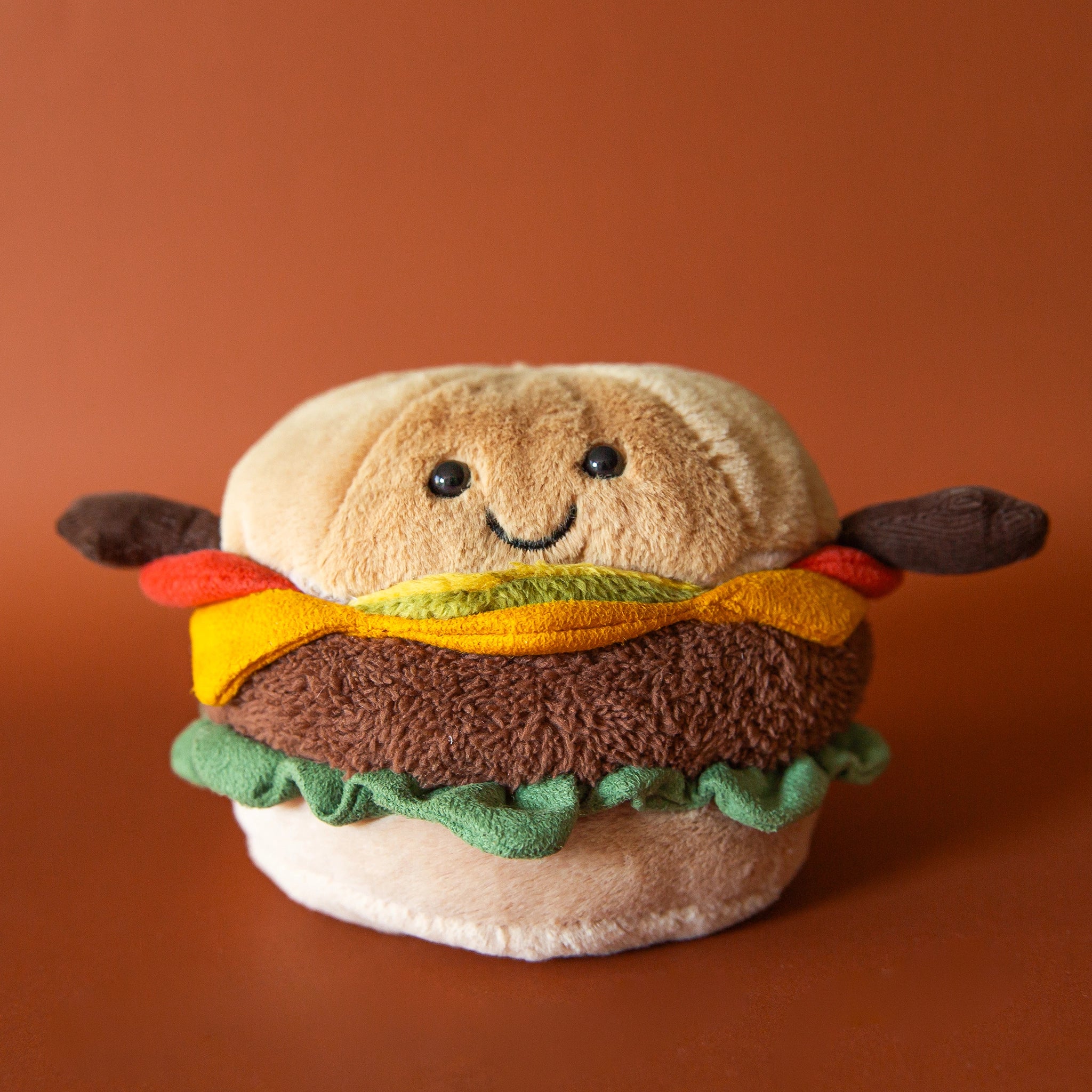On a brown background is a stuffed burger toy with a smiling face.