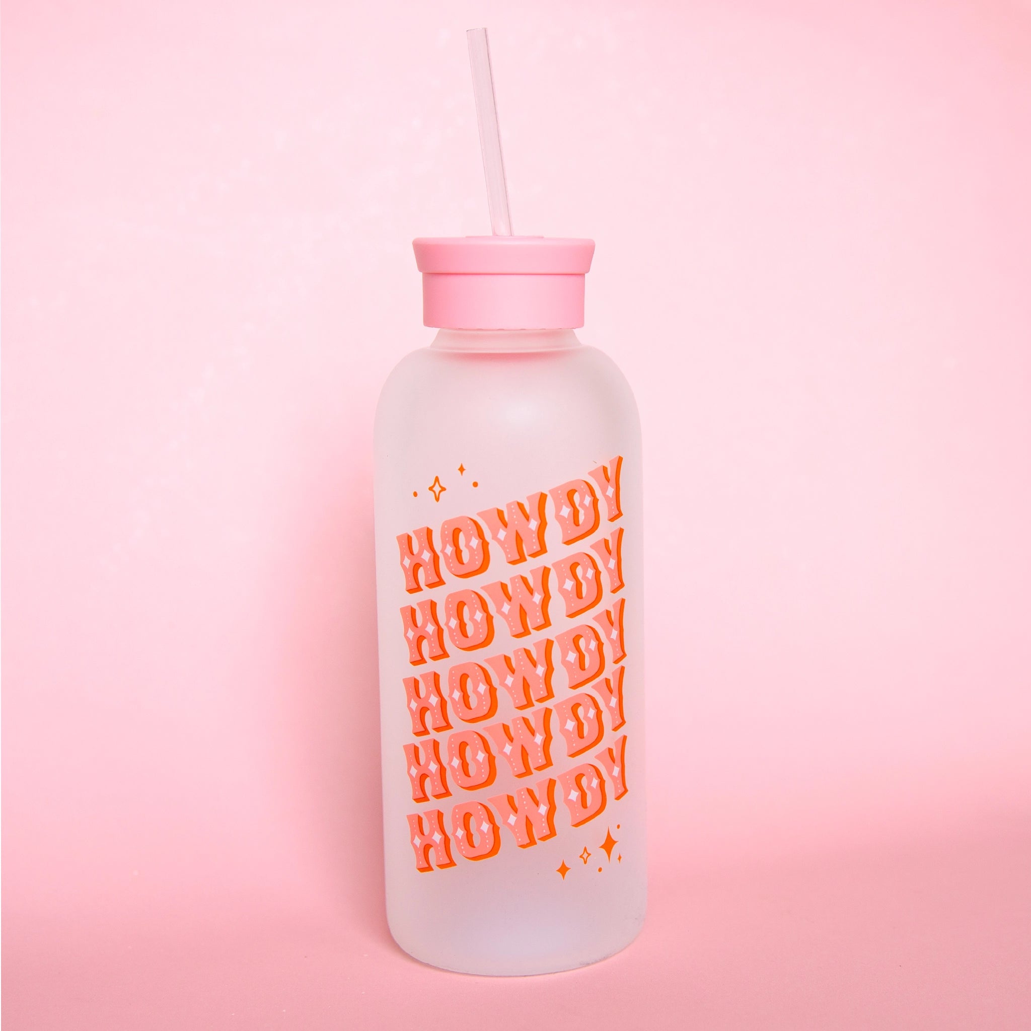 A glass water bottle with the word "HOWDY" in pink western style letters ,stacked five times at an angle on the front, a pink silicone lid with a straw coming out of the top.