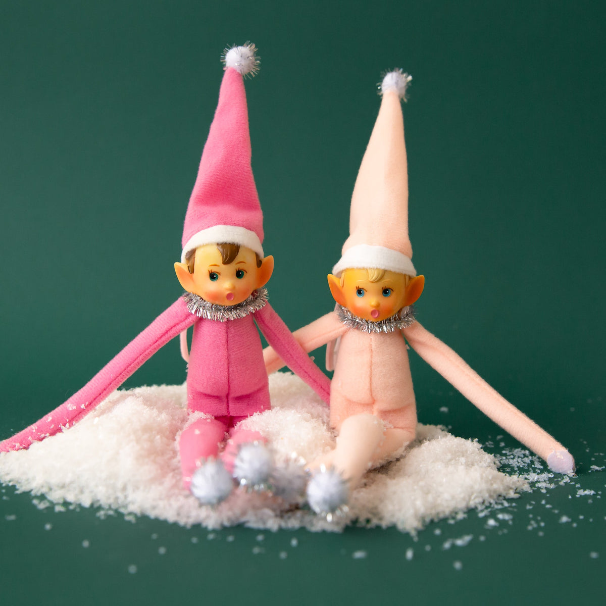 Two pink elf ornaments sitting in a pile of white snow.