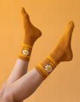 On a peachy background is a burnt orange pair of socks with a daisy graphic on the sides.