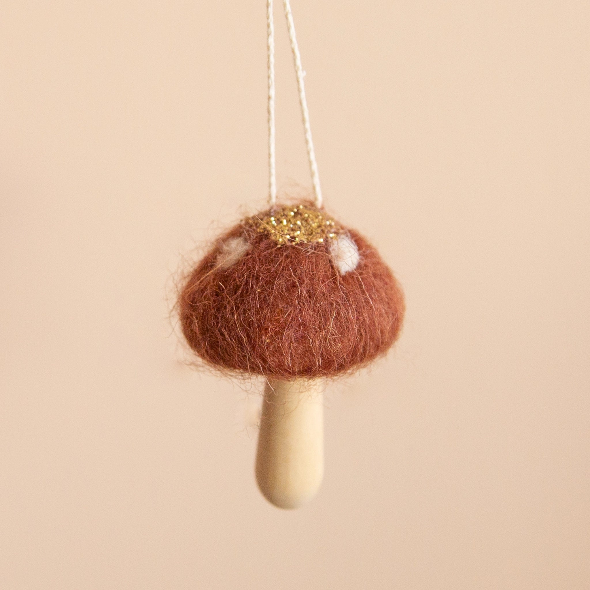 A cocoa colored mushroom ornament with white spots and a light wood stem.