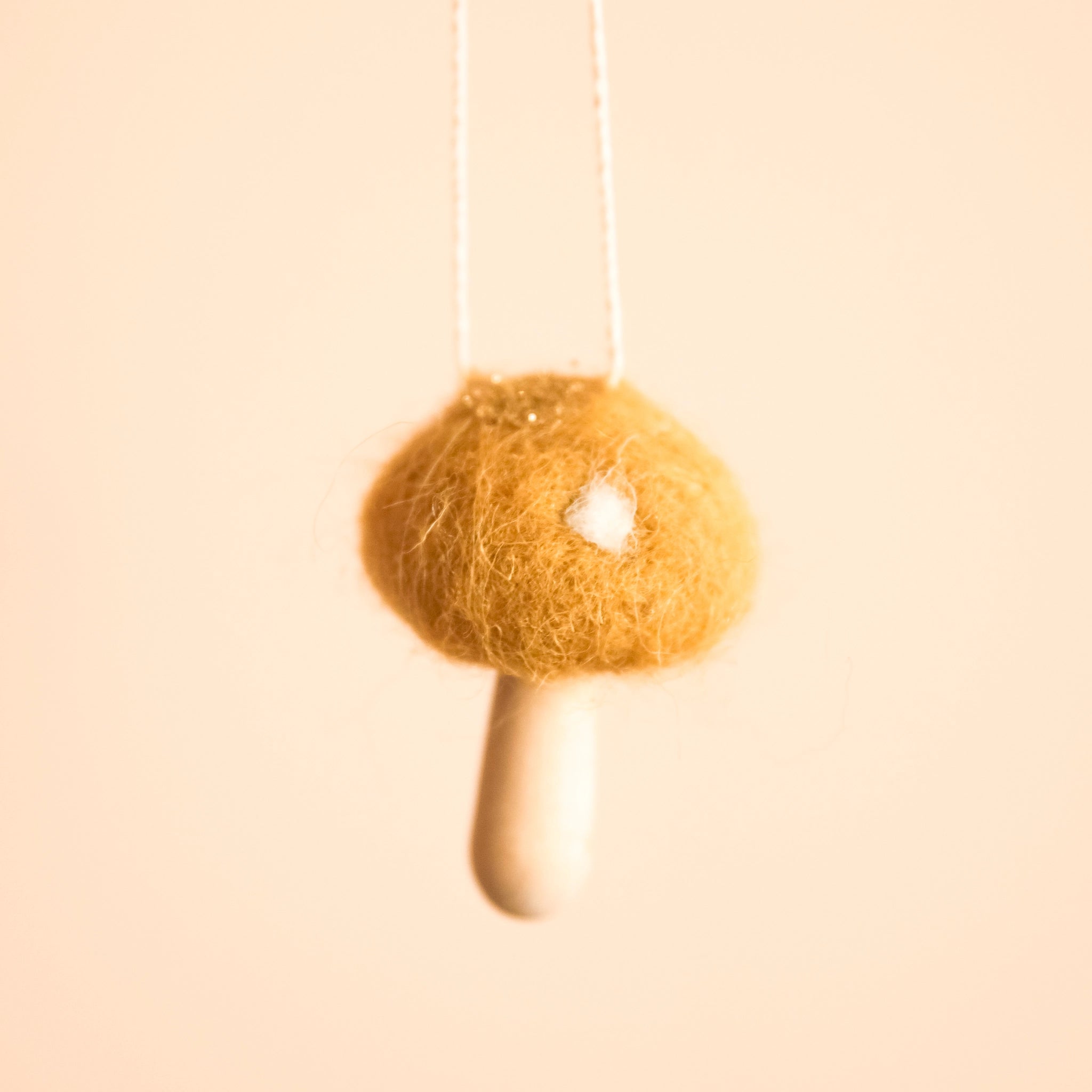A yellow wool mushroom ornament with white spots and a light wood stem.