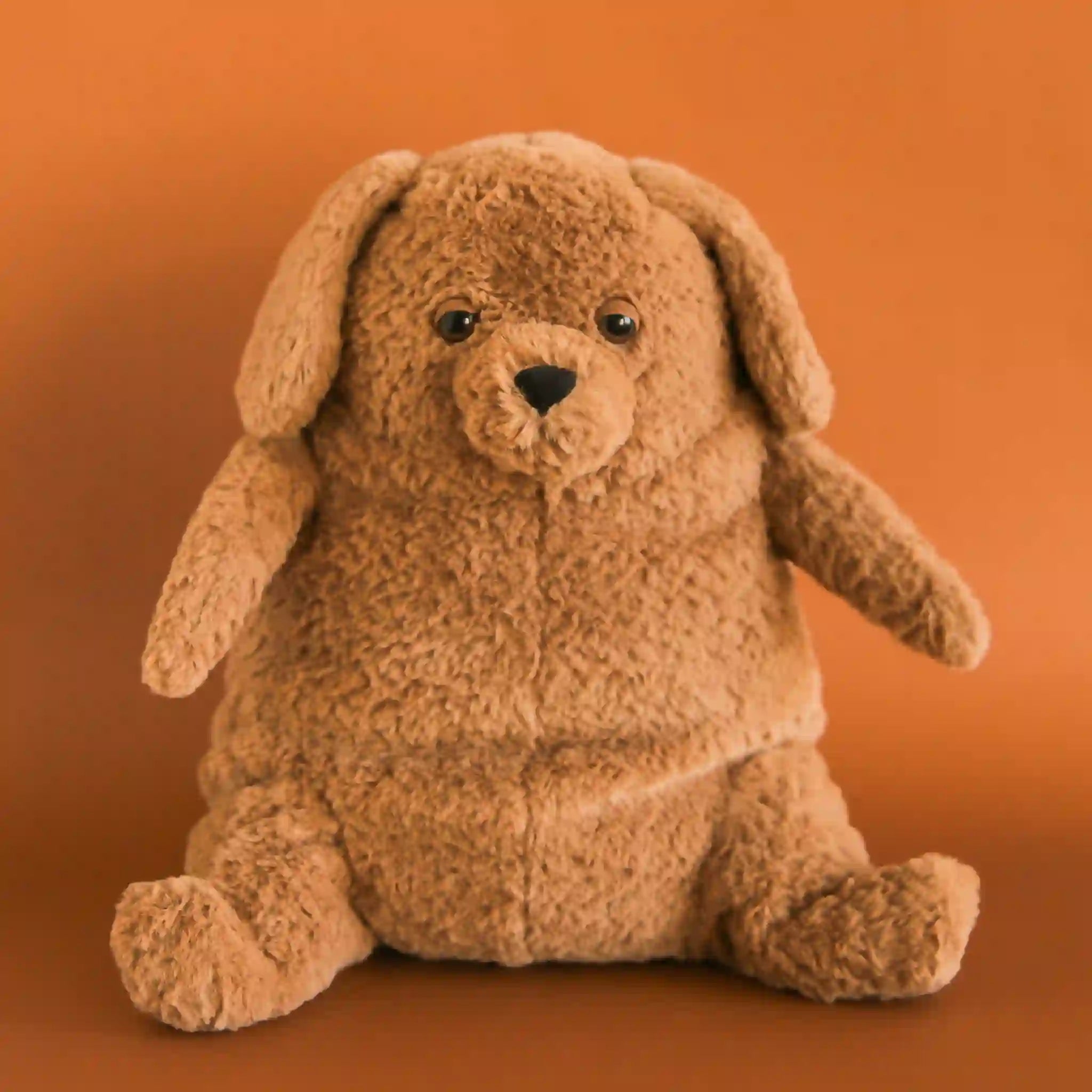 On an orange background is a snuggly brown stuffed animal dog with sleepy eyes and a chunky figure.