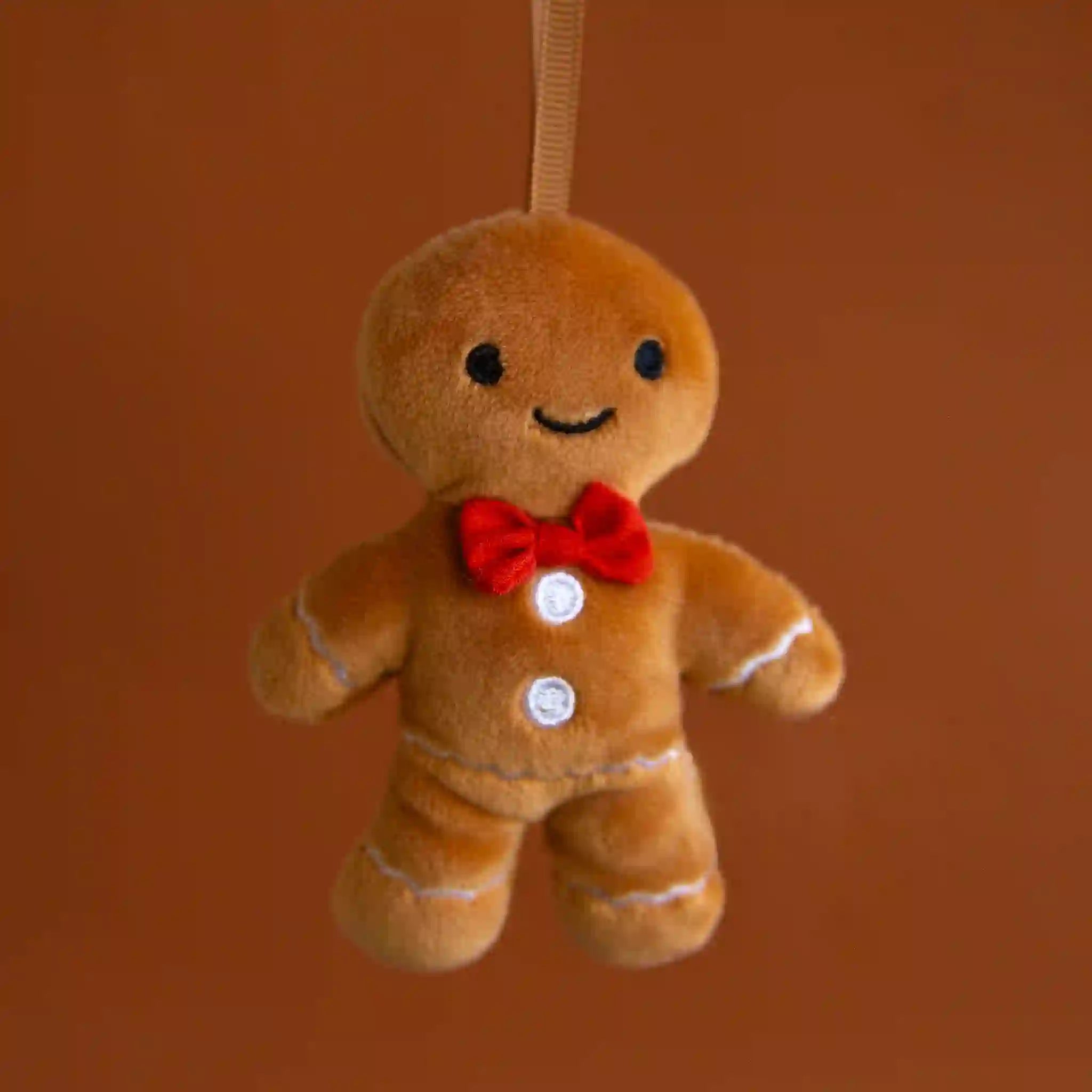 On a brown background is a stuffed toy gingerbread man with white detailing and a red bowtie.