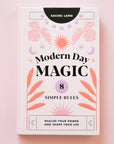 A light pink book cover with pink, lavender and orange foliage and sun and moon graphics along with black text that reads, "Modern Day Magic 8 Simple Rules Realize Your Power and Shape Your Life".