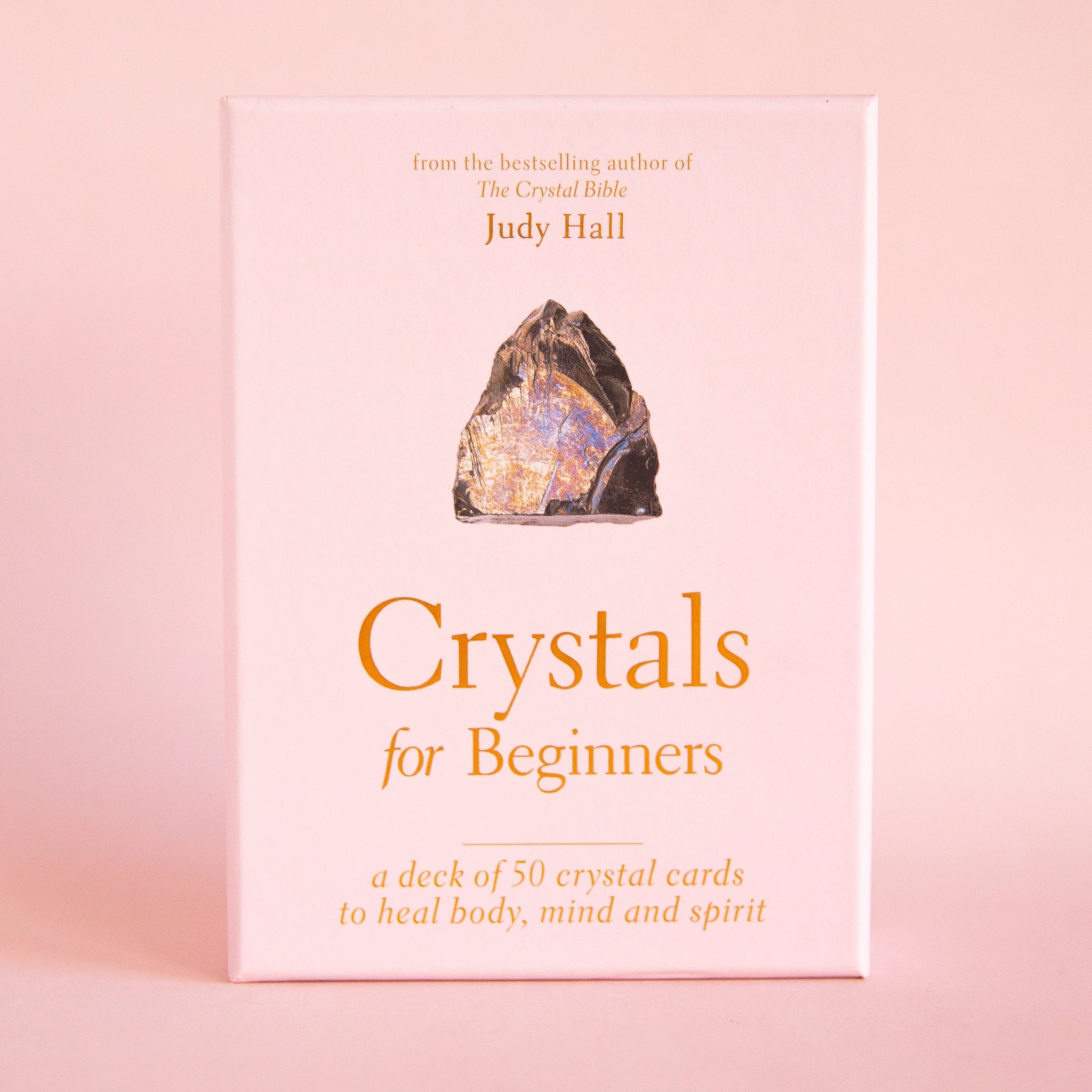 A deck of cards with a cover that has a crystals and text that reads, "Crystals for Beginners, a deck of 50 crystal cards to heal body, mind and spirit" in mustard yellow writing.
