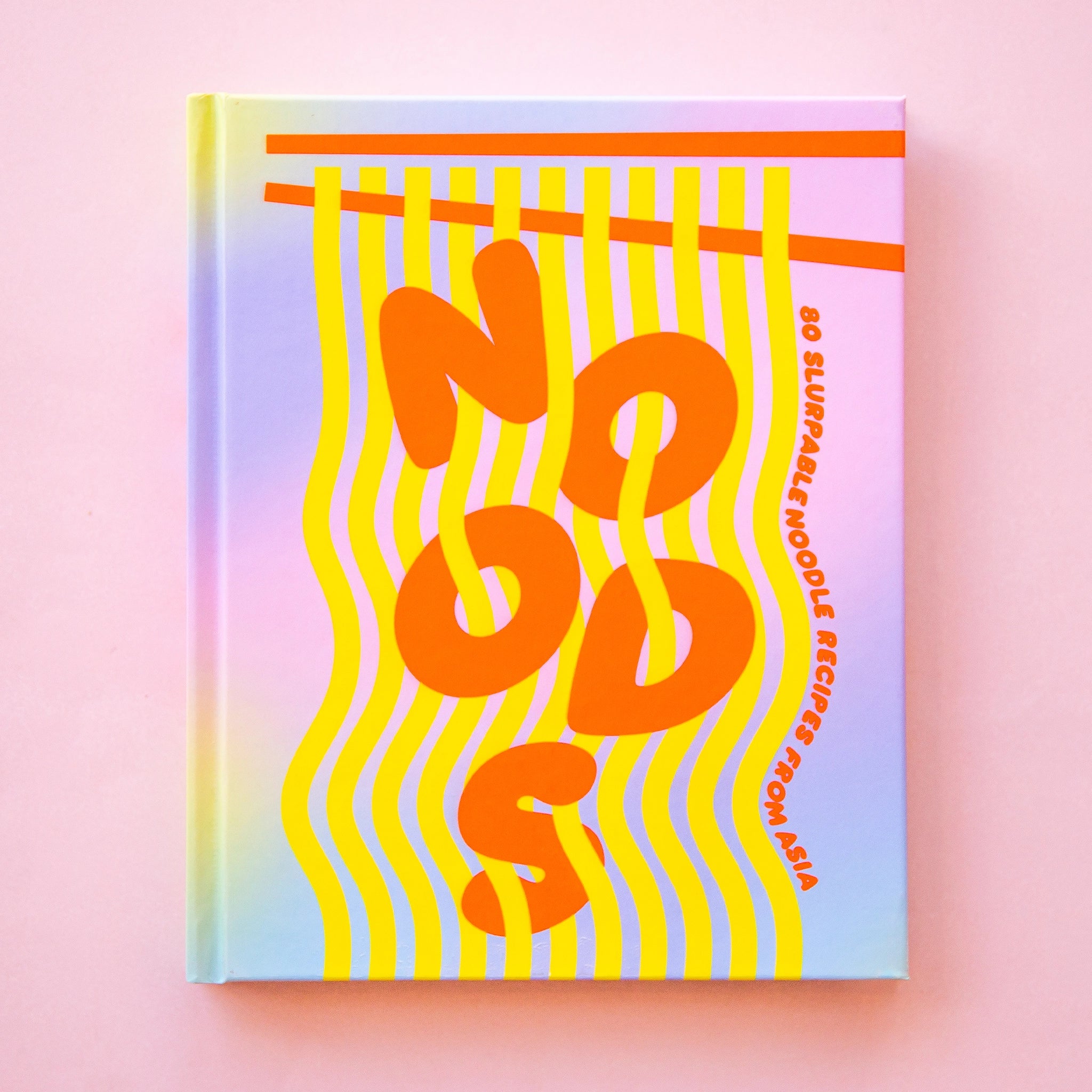 On a neutral background is a ombre purple, blue and pink cookbook cover with bright orange letters that read, "Noods 80 Slurpable Noodle Recipes From Asia".