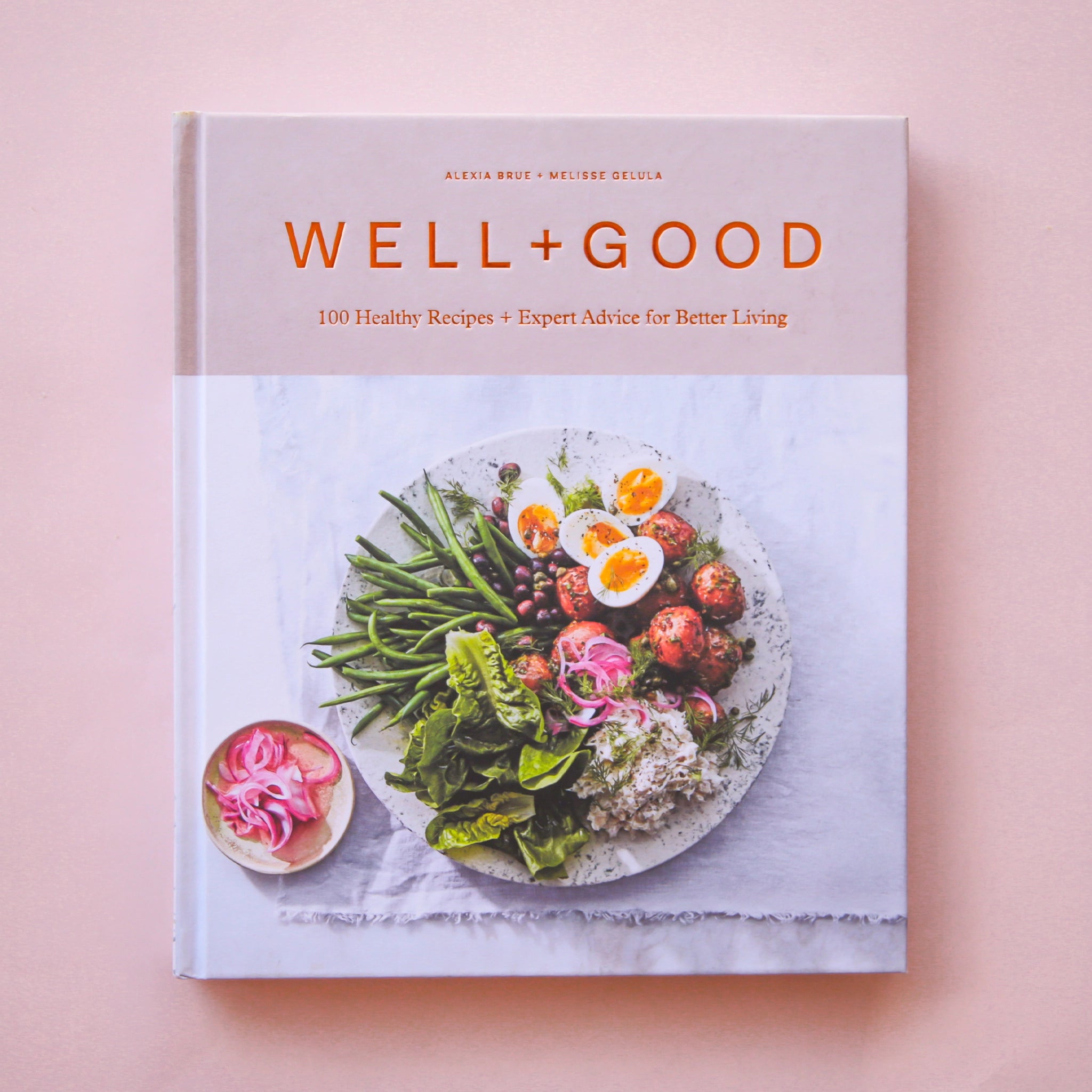 Hard cover cookbook titled &#39;Well + Good, 100 healthy recipes + expert advice for better living&#39; in gold lettering. Below the title is a beautifully plated salad of greens, eggs, rice and more.