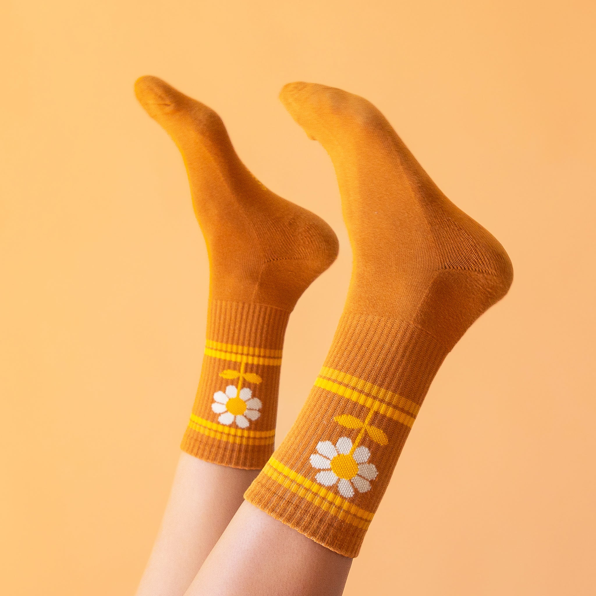 On a peachy background is a burnt orange pair of socks with a daisy graphic on the sides.