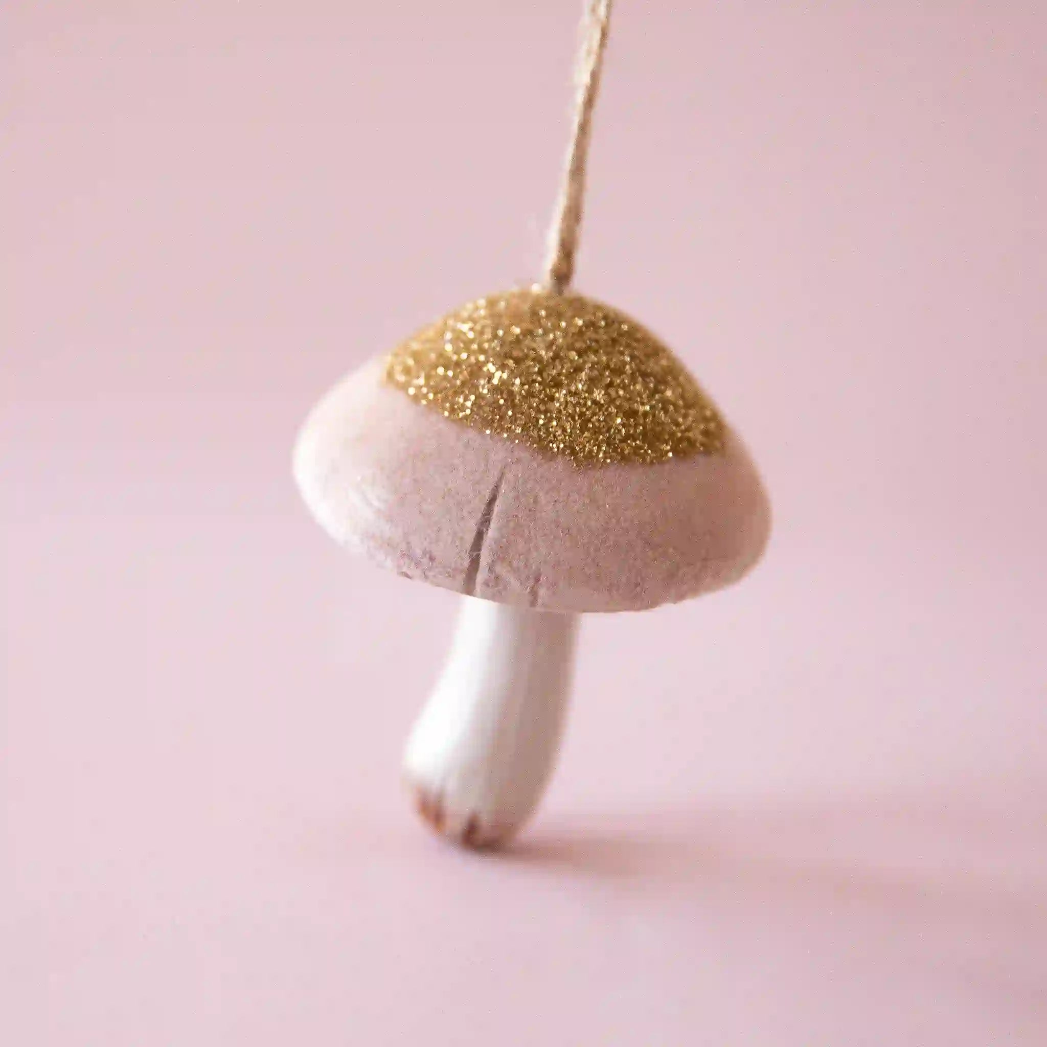 On a pink background is a light pink mushroom ornament with a gold glitter top. 