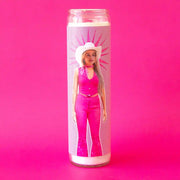 On a hot pink background is a prayer candle with a picture of margot robbie as Barbie wearing a bright pink cowgirl outfit. 